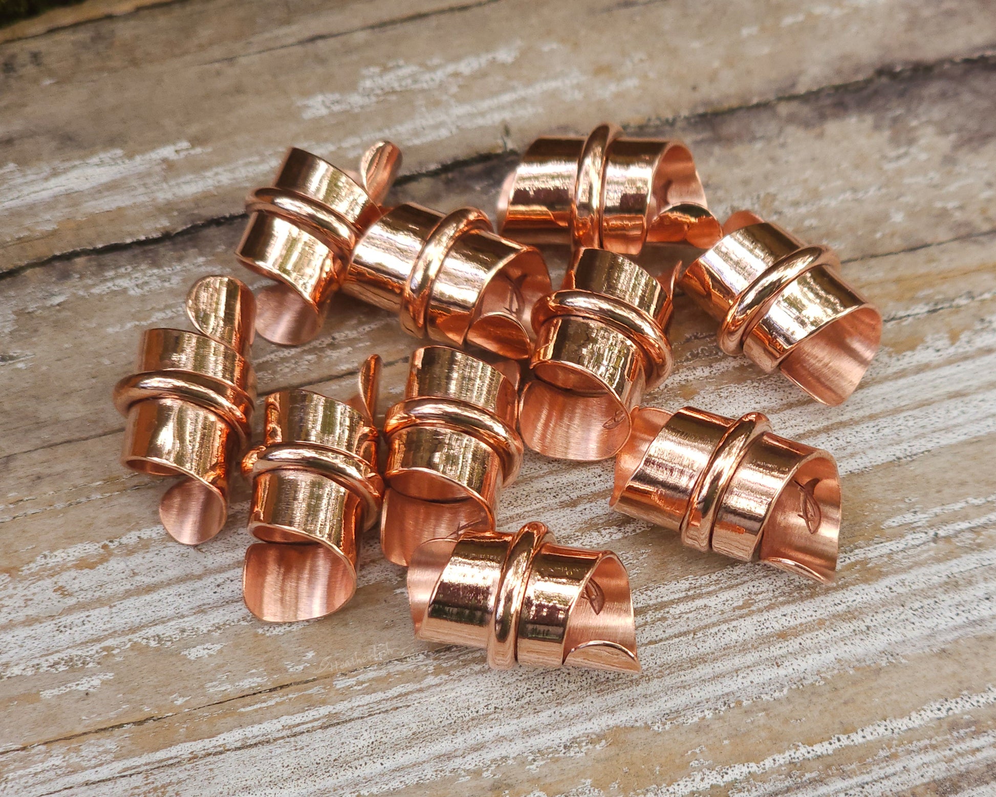 Copper hair jewelry for locs, dreadlocks, braids, or beards, stylized with a center ring and flattened ends, displayed on a wood background.