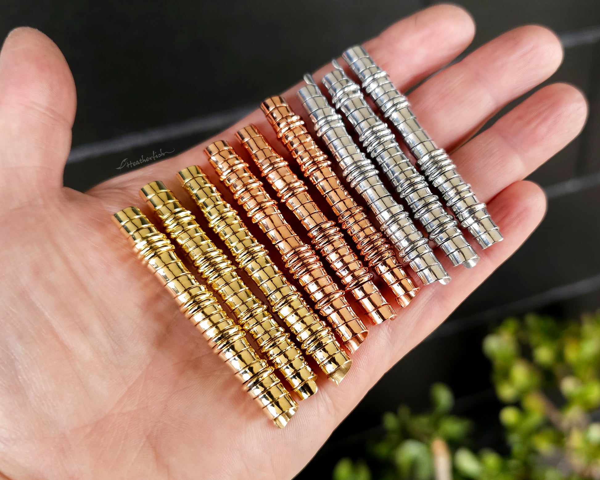 A set of brass, copper, and aluminum dreadlock beads held in hand to show scale.