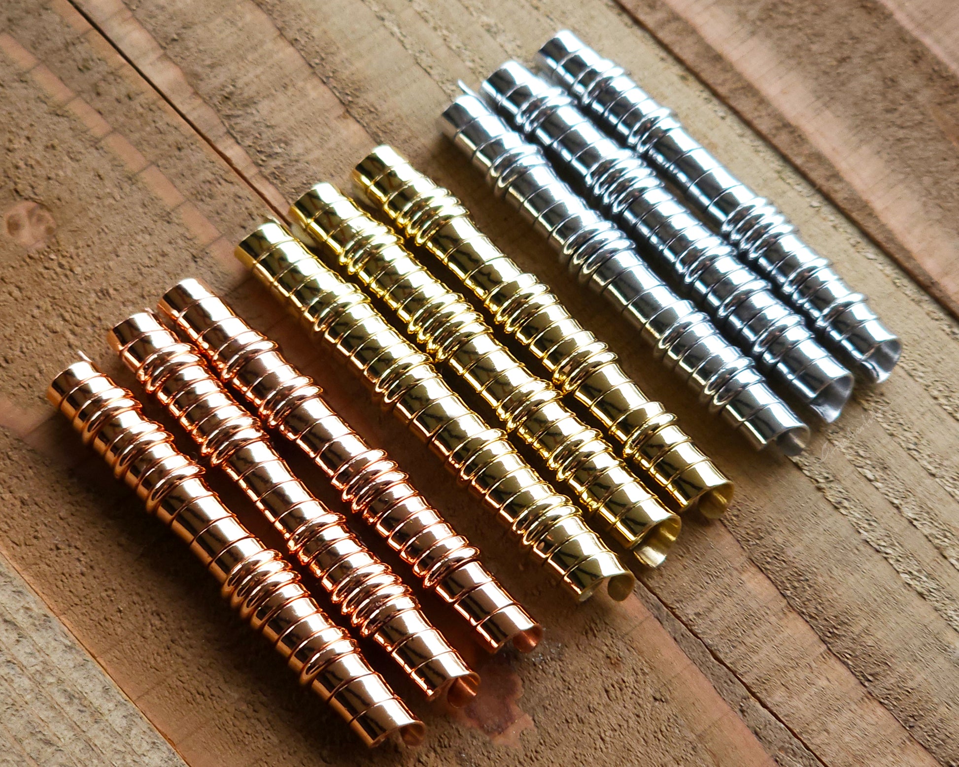 A set of brass, copper, and aluminum dreadlock beads on a wood surface.