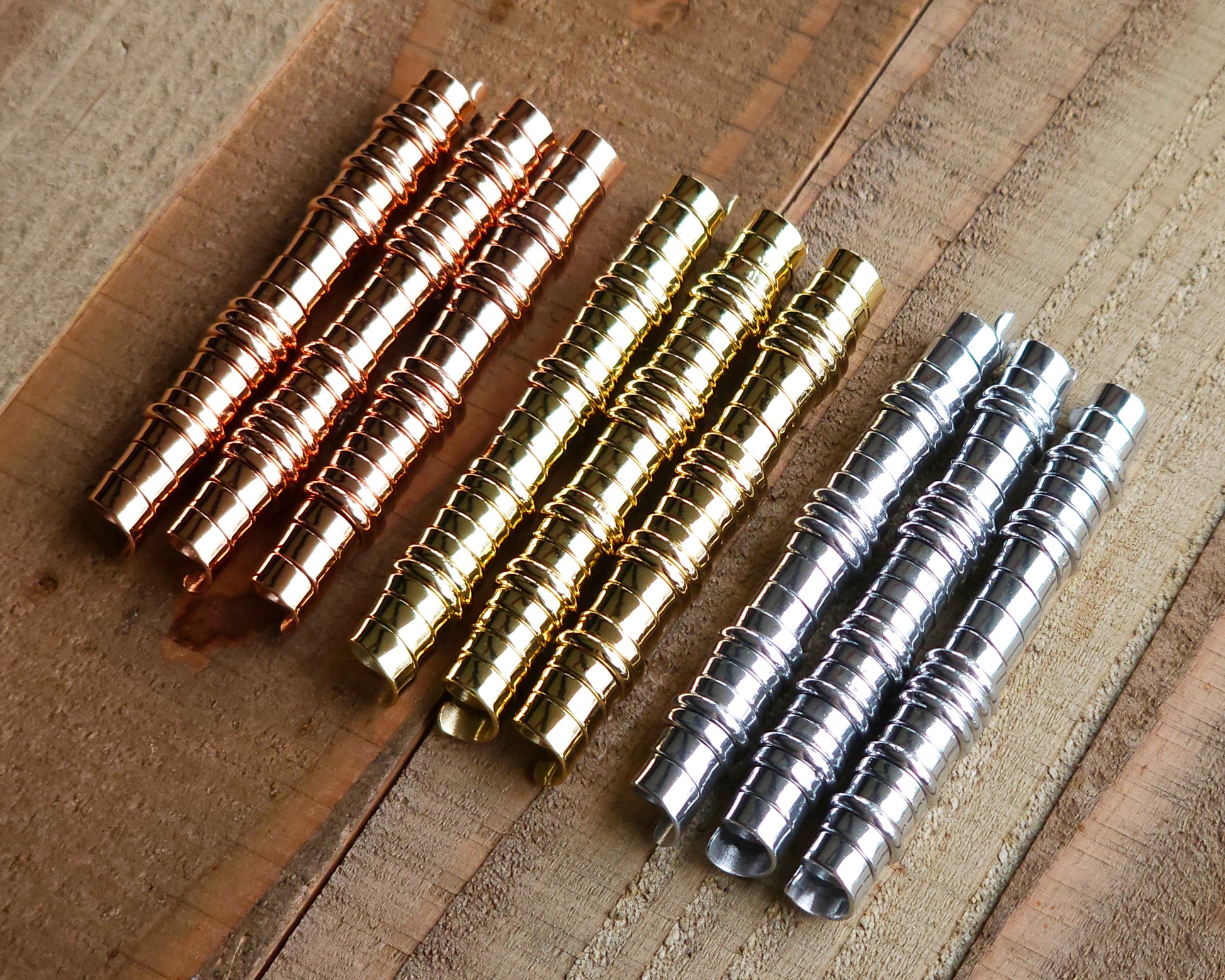 A set of brass, copper, and aluminum loc beads on a wood surface.