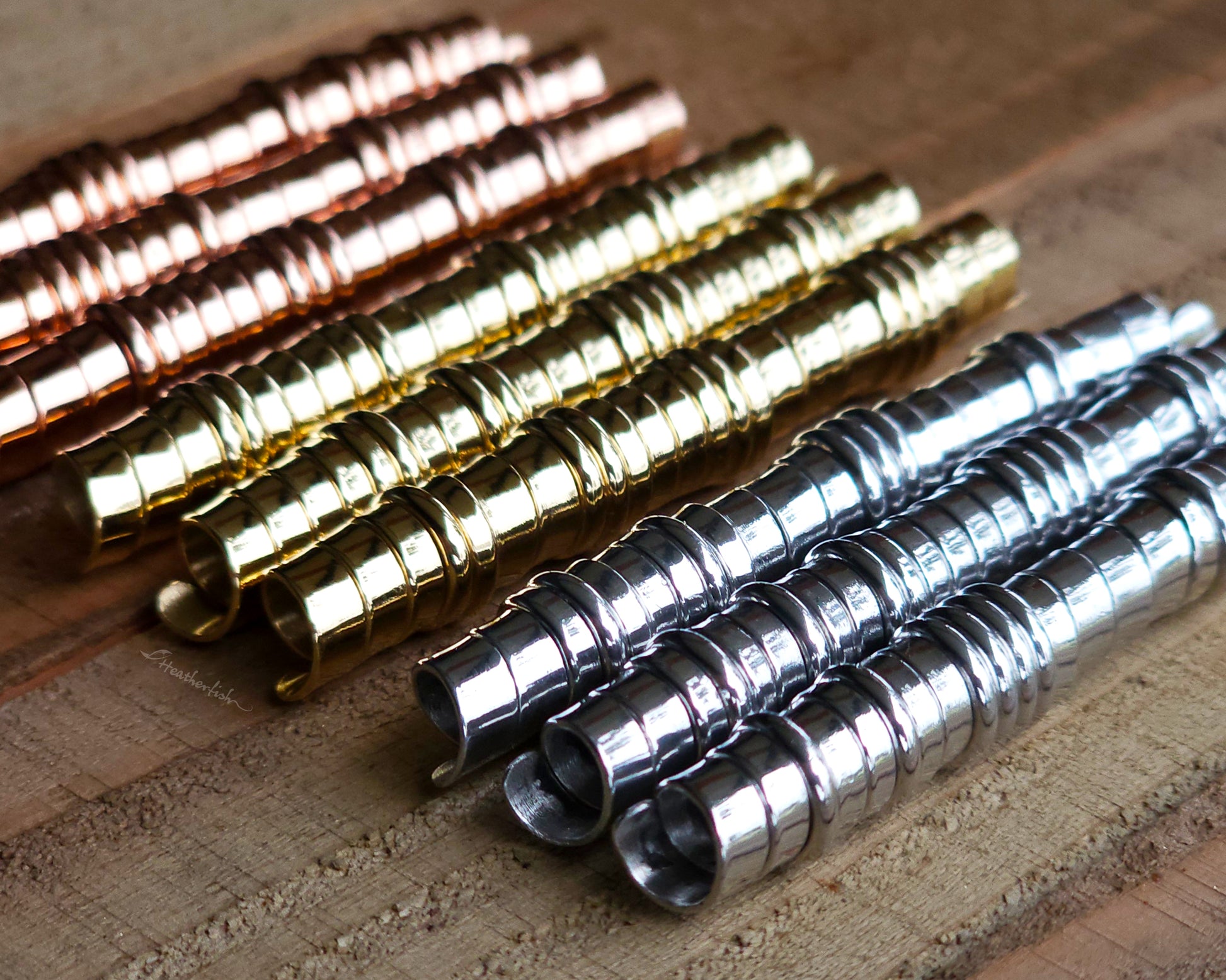 A set of brass, copper, and aluminum hair coils on a wood surface.