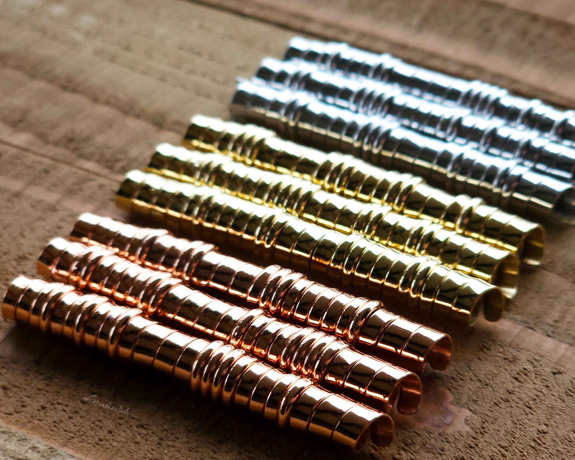 A set of brass, copper, and aluminum hair coils on a wood surface.