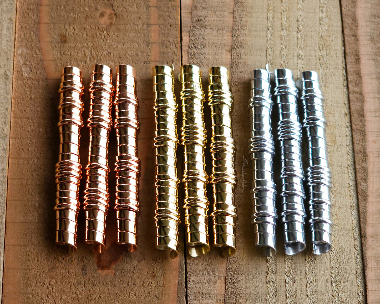 A set of brass, copper, and aluminum hair coils on a wood surface.