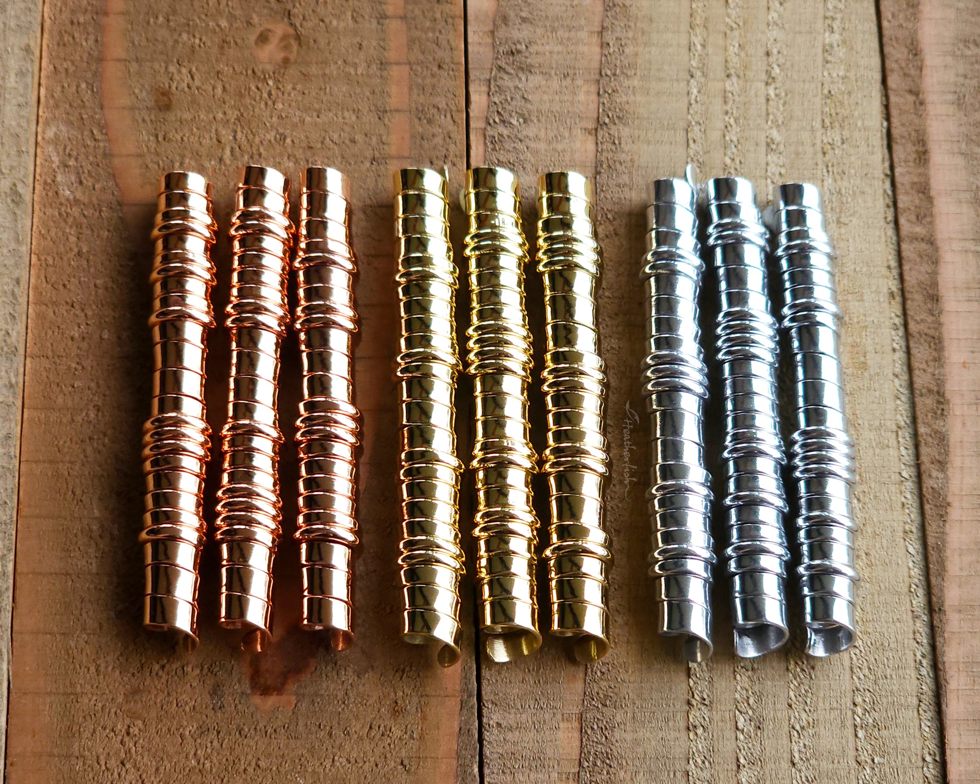 A set of brass, copper, and aluminum hair coils on a wood surface.