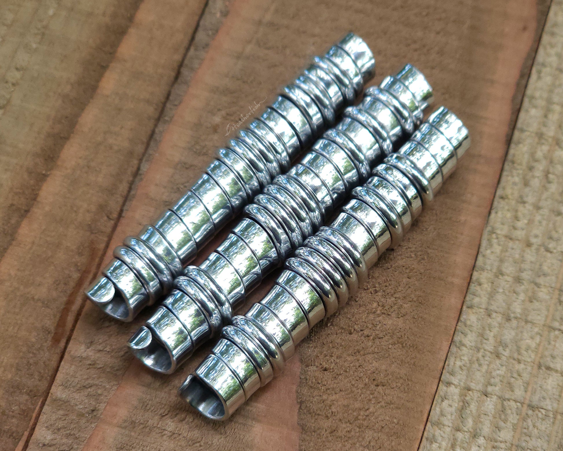 Three aluminum hair beads on a wood surface.