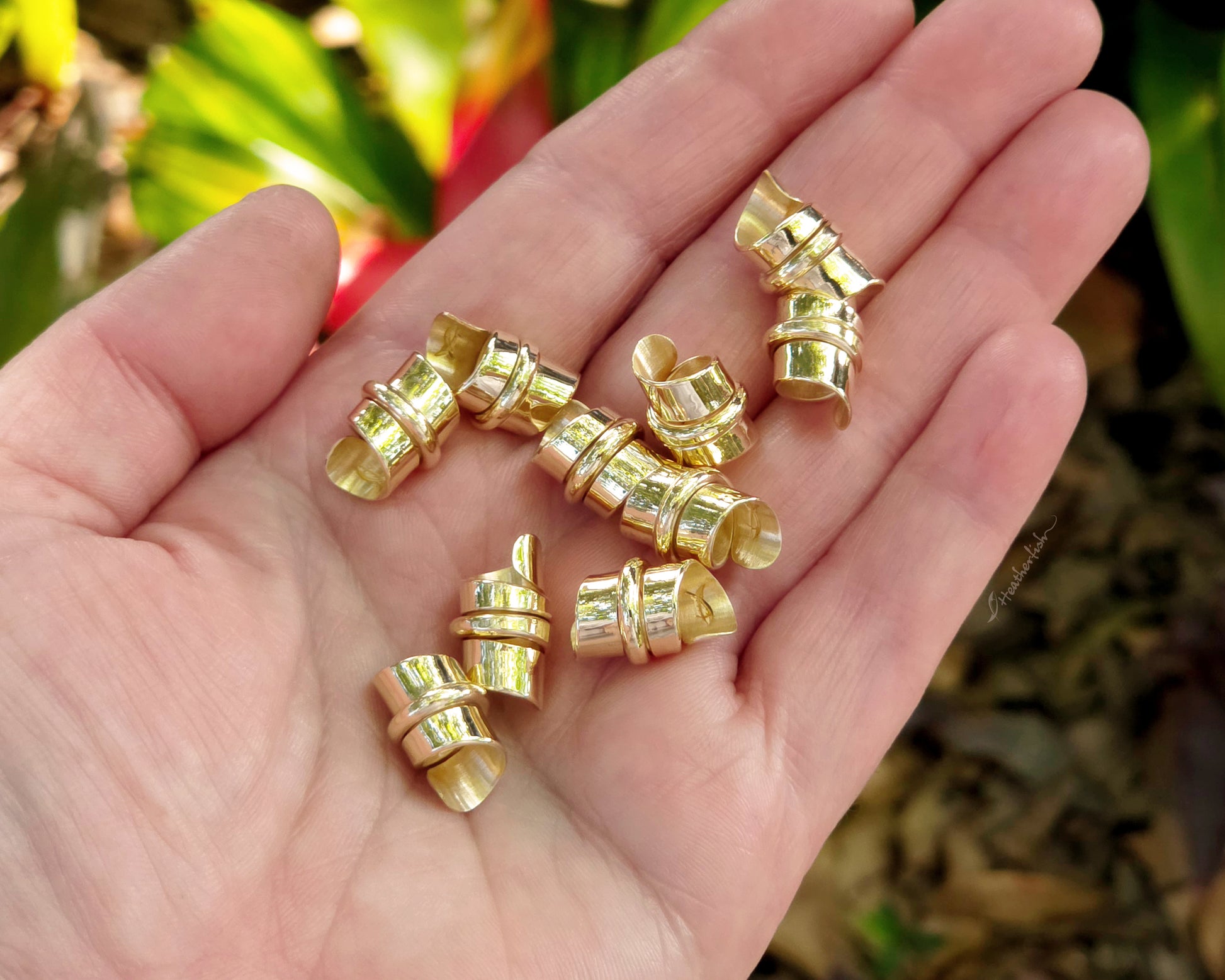 Red brass hair beads held in a hand with a natural background in the background.