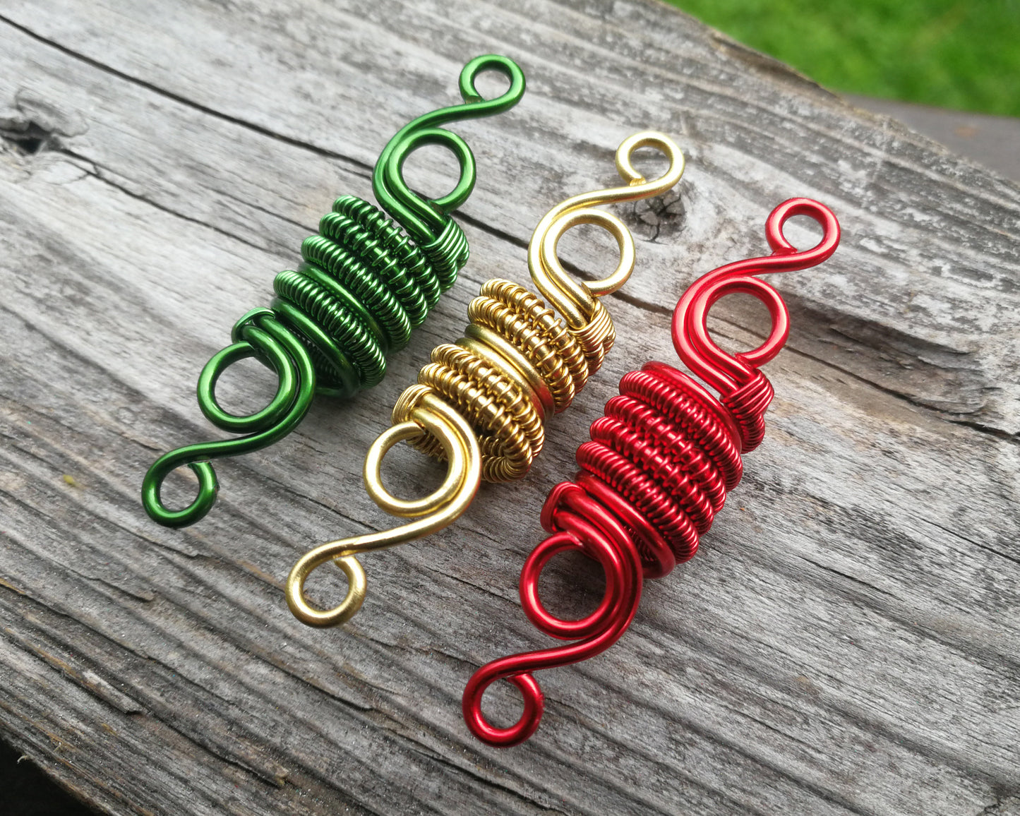 Three woven loc beads in green, gold, and red on a wood background.