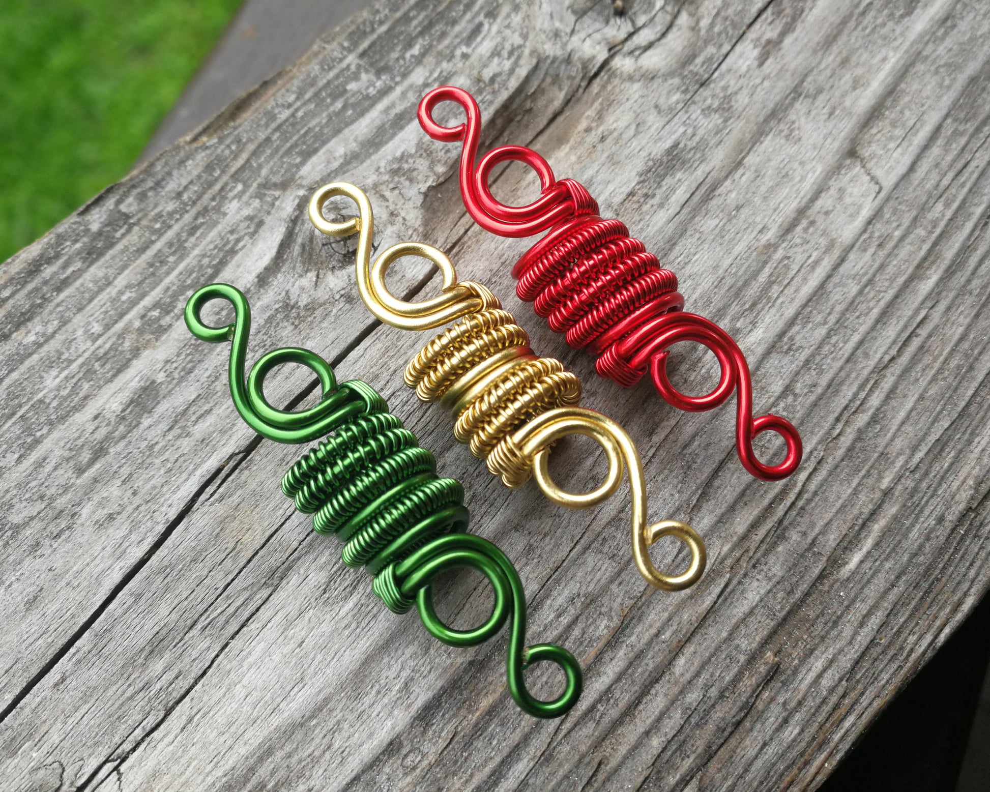 Three woven loc beads in green, gold, and red on a wood background.