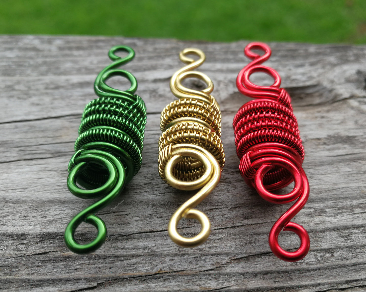 Three woven loc beads in green, gold, and red on a wood background.