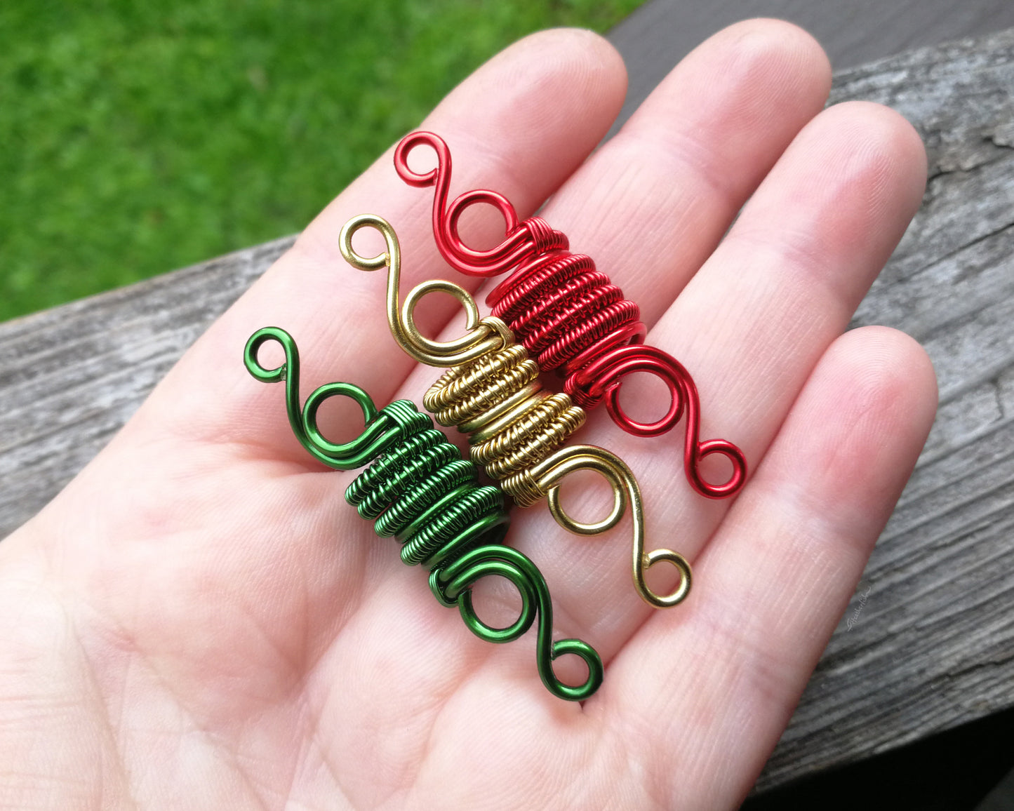 Three woven loc beads in green, gold, and red held in a hand to show scale.