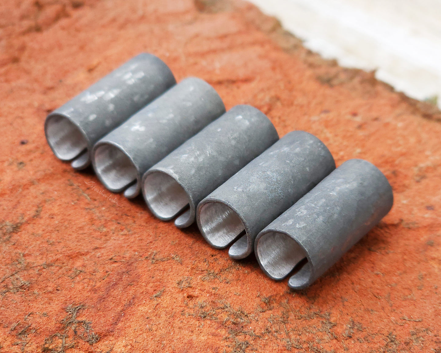 Set of 5 textured oxidized aluminum hair cuffs for locs, dreadlocks, braids, or beards, in a matte grey. Sitting on a reddish orange brick lined up in a row.