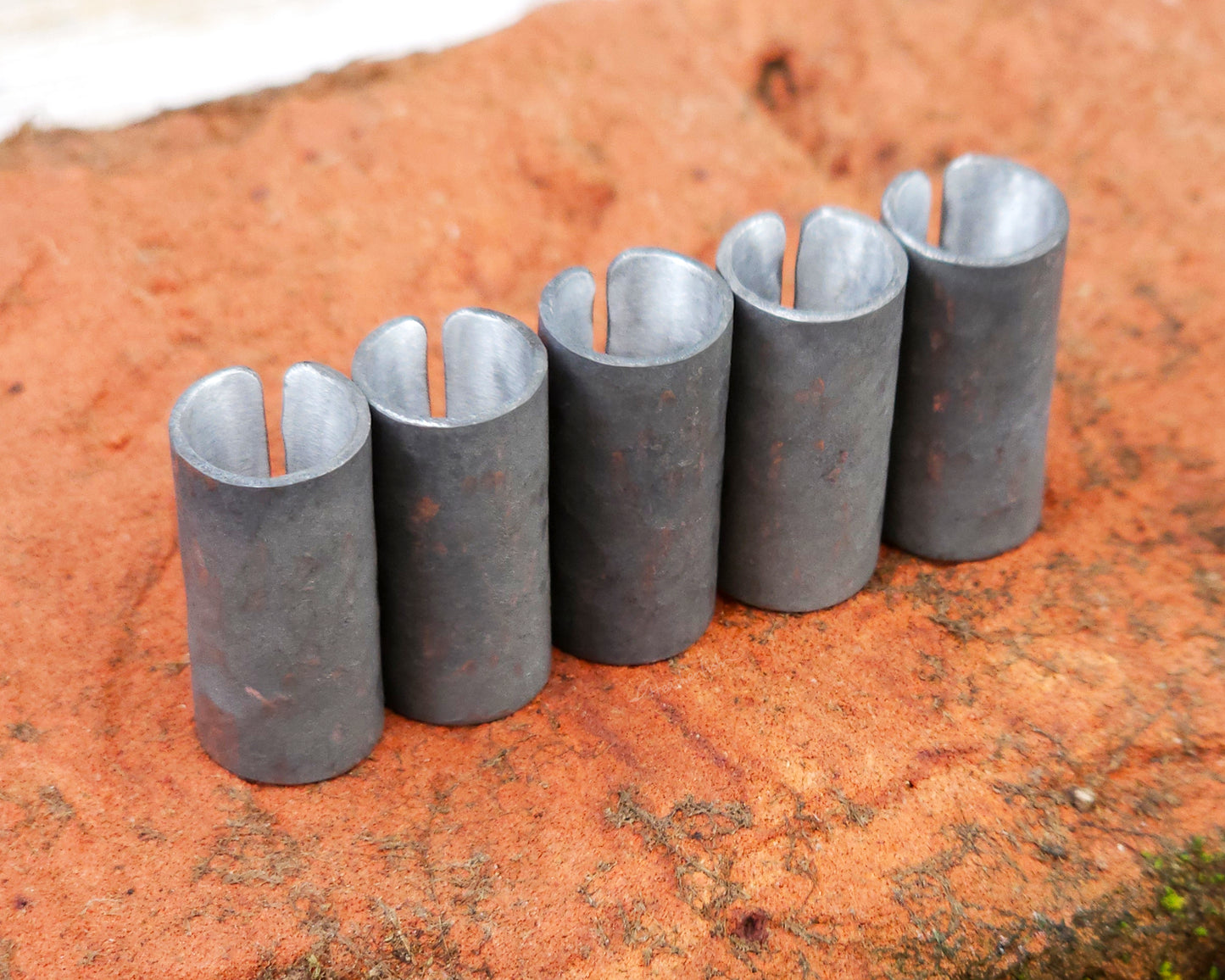 Set of 5 textured oxidized aluminum hair cuffs for locs, dreadlocks, braids, or beards, in a matte grey. Sitting on a reddish orange brick lined up in a row.