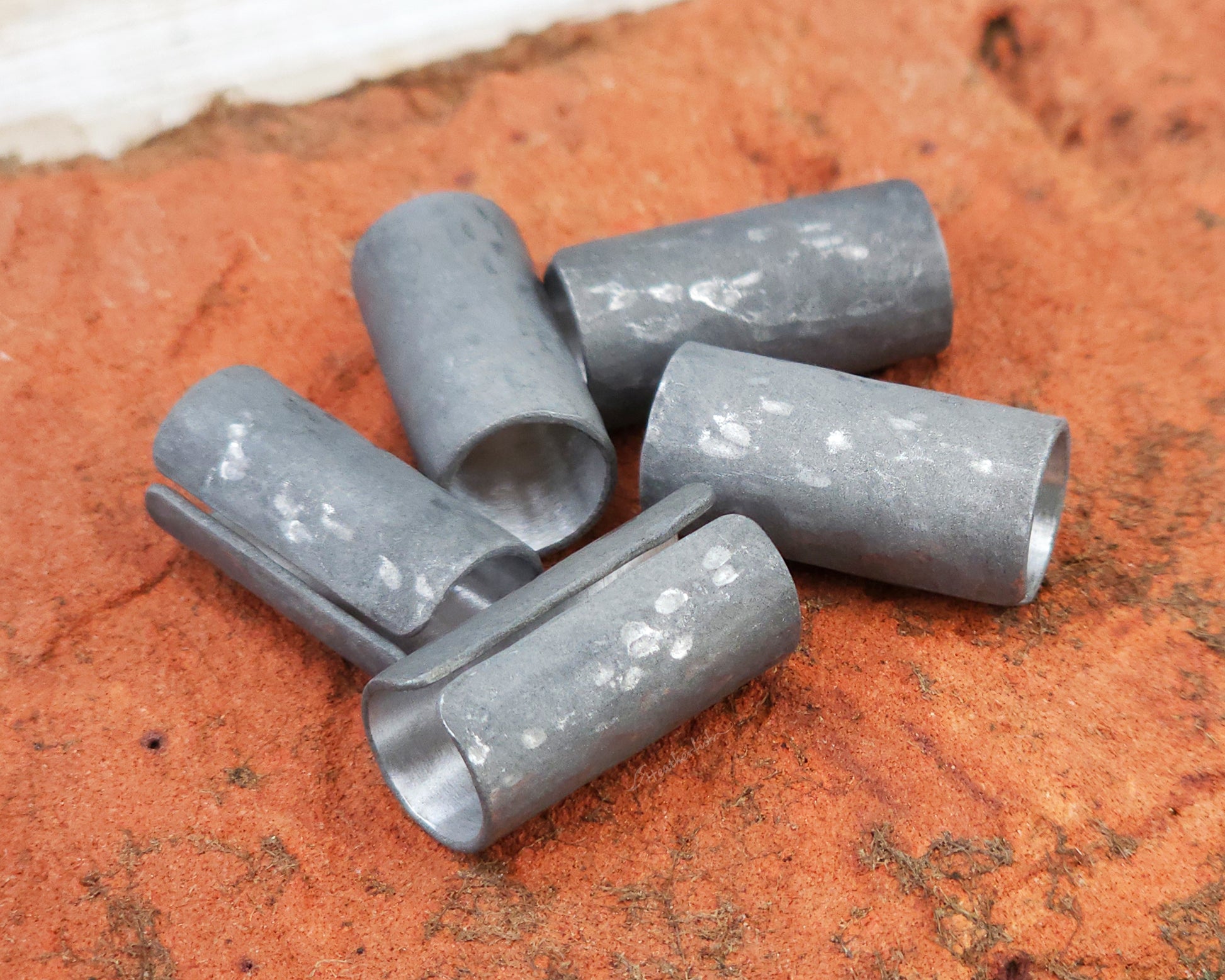 Set of 5 textured oxidized aluminum hair cuffs for locs, dreadlocks, braids, or beards, in a matte grey. Sitting on a reddish orange brick lined up in a random pile.