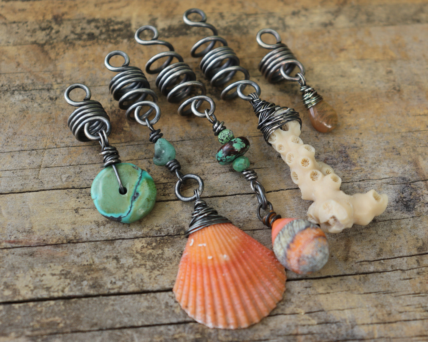 A set of five silver hair coils featuring an orange shell, white coral, orange artisan lampwork glass, Hubei Turquoise, aquamarine, and a Welo Ethiopian Opal.