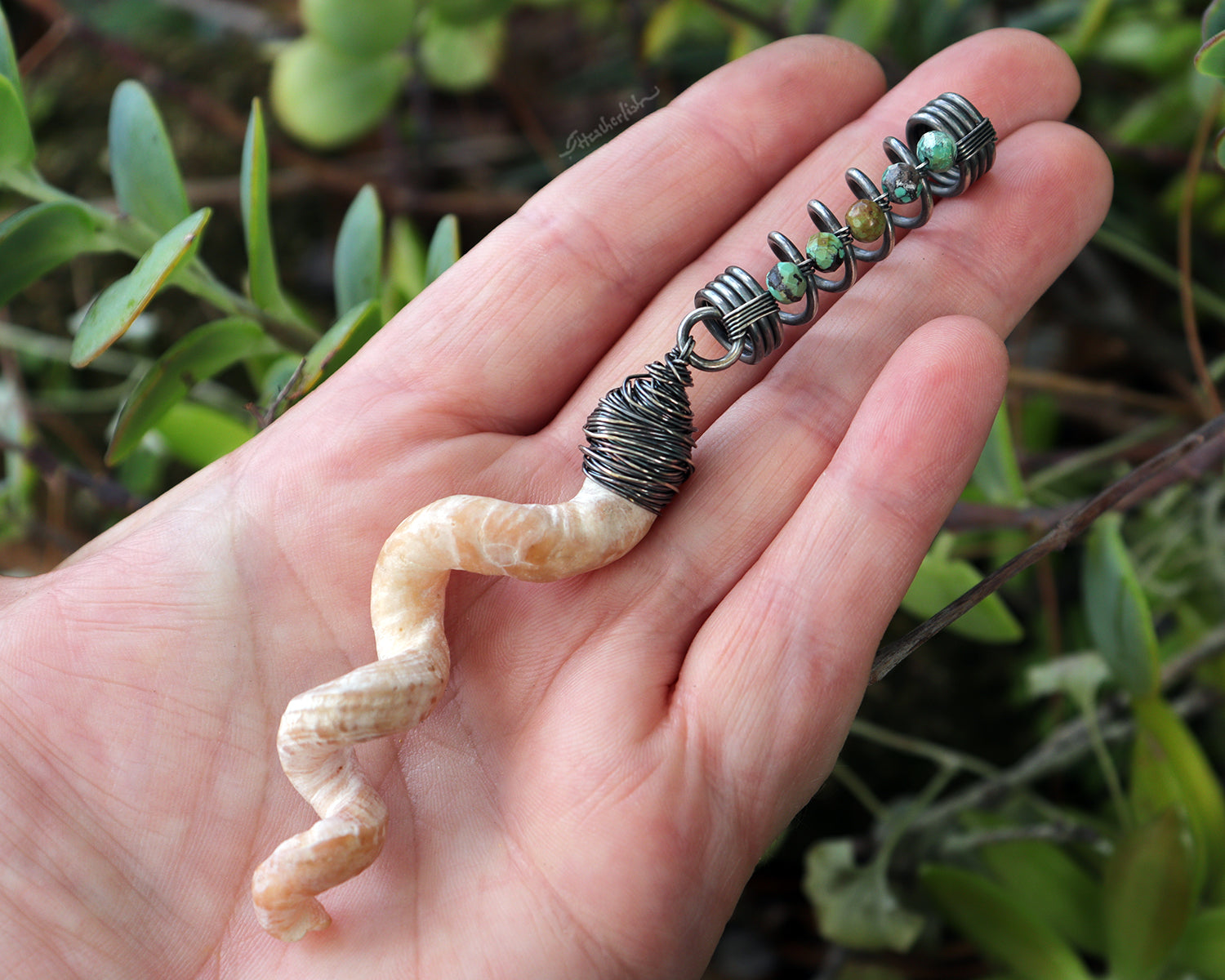 Hair jewelry featuring a silver coil accented with Hubei Turquoise beads and the spiral sea shell from a Florida tube snail, held in hand to show scale.