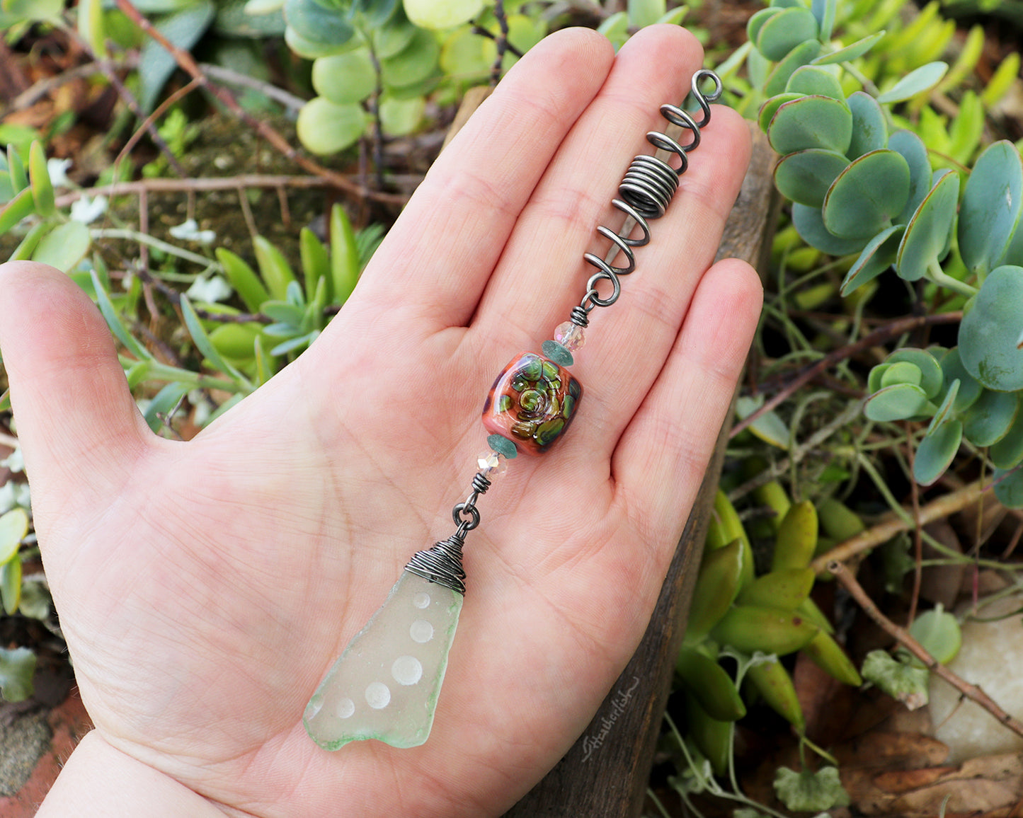 Hair Jewelry featuring a coral/raku lampwork glass bead and carved sea glass on a silver coil held in hand to show scale.