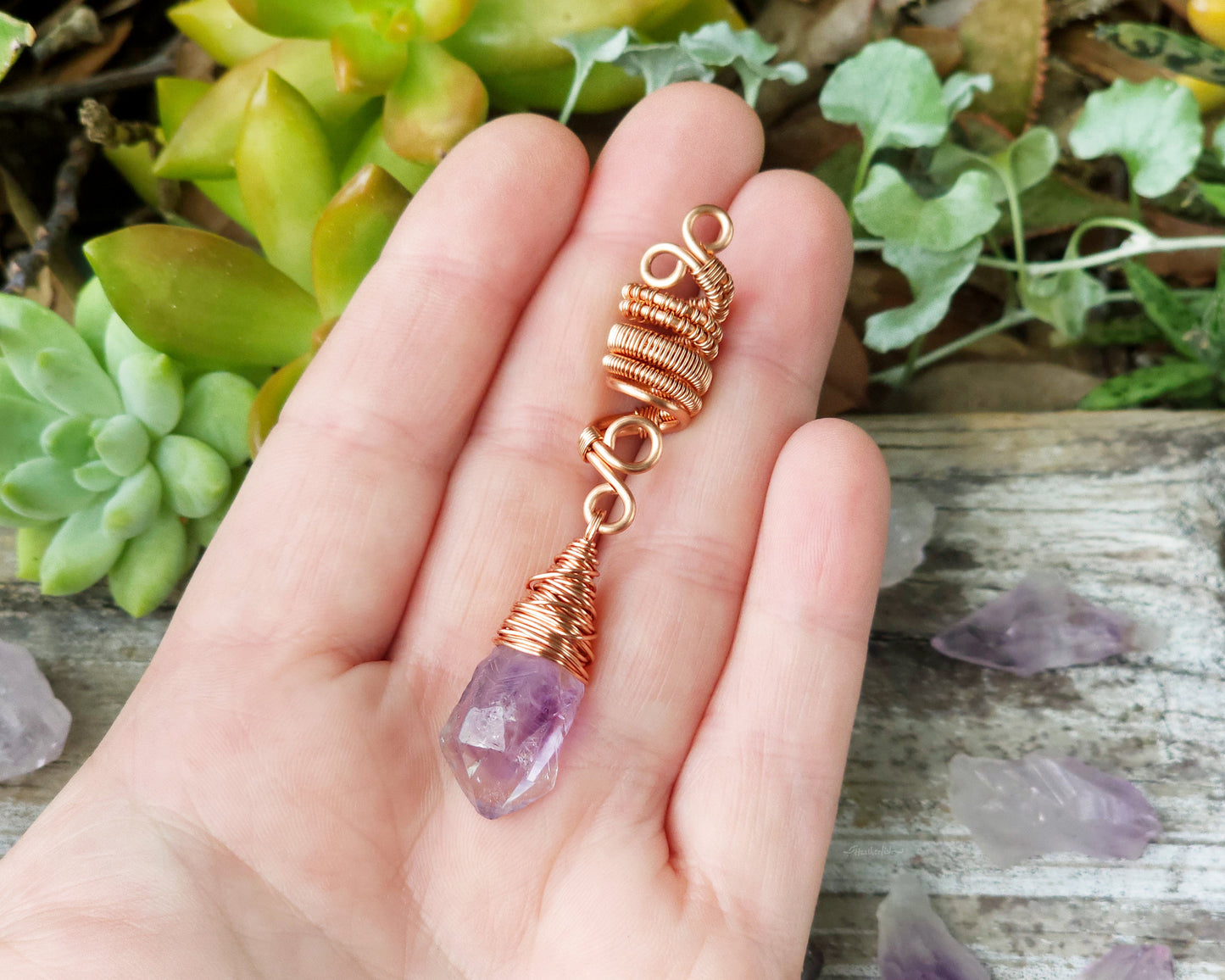 A woven copper dread bead featuring a raw Arkansas amethyst crystal point and held in hand to show scale.