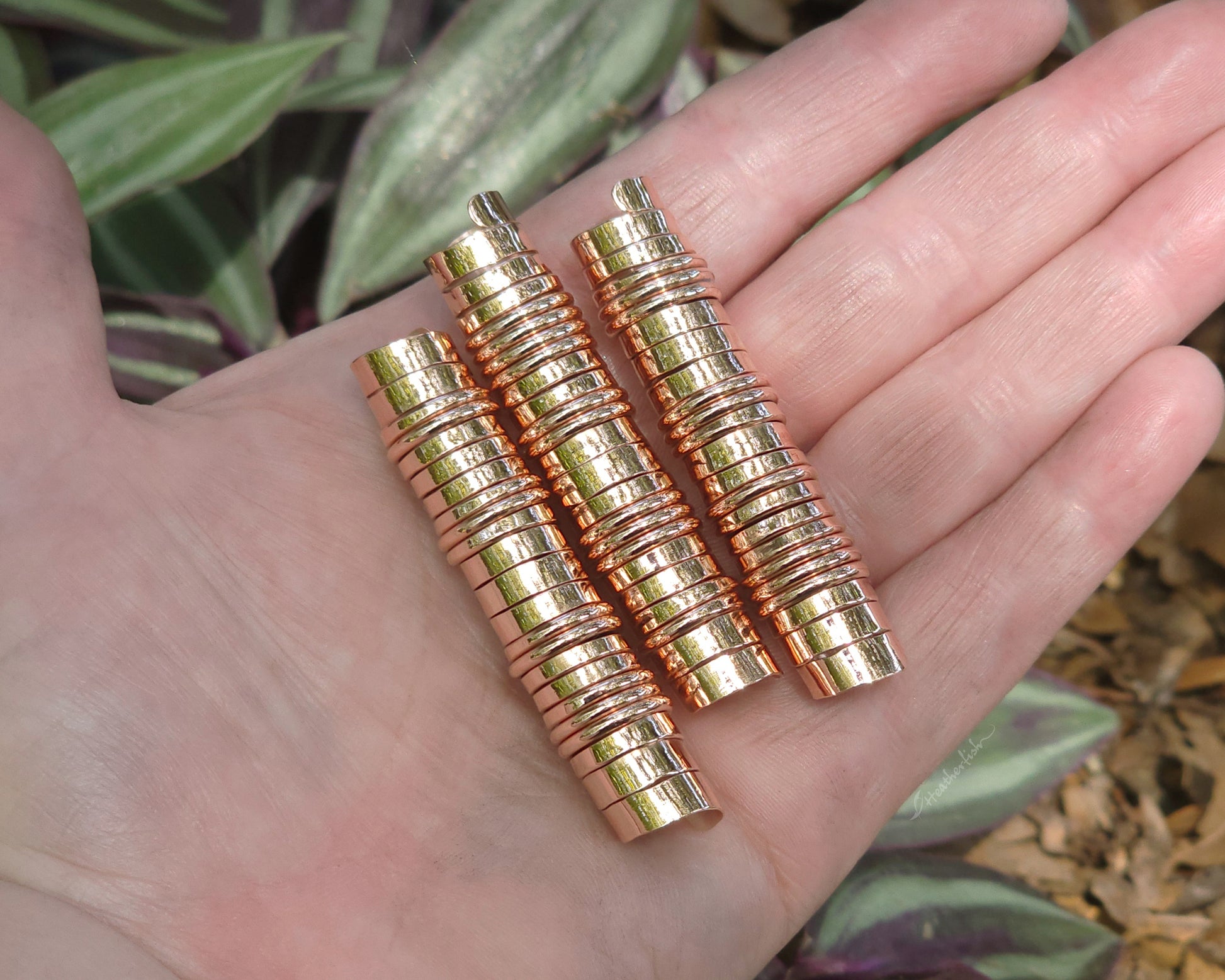 Three extra long copper hair coils held in hand to show scale.