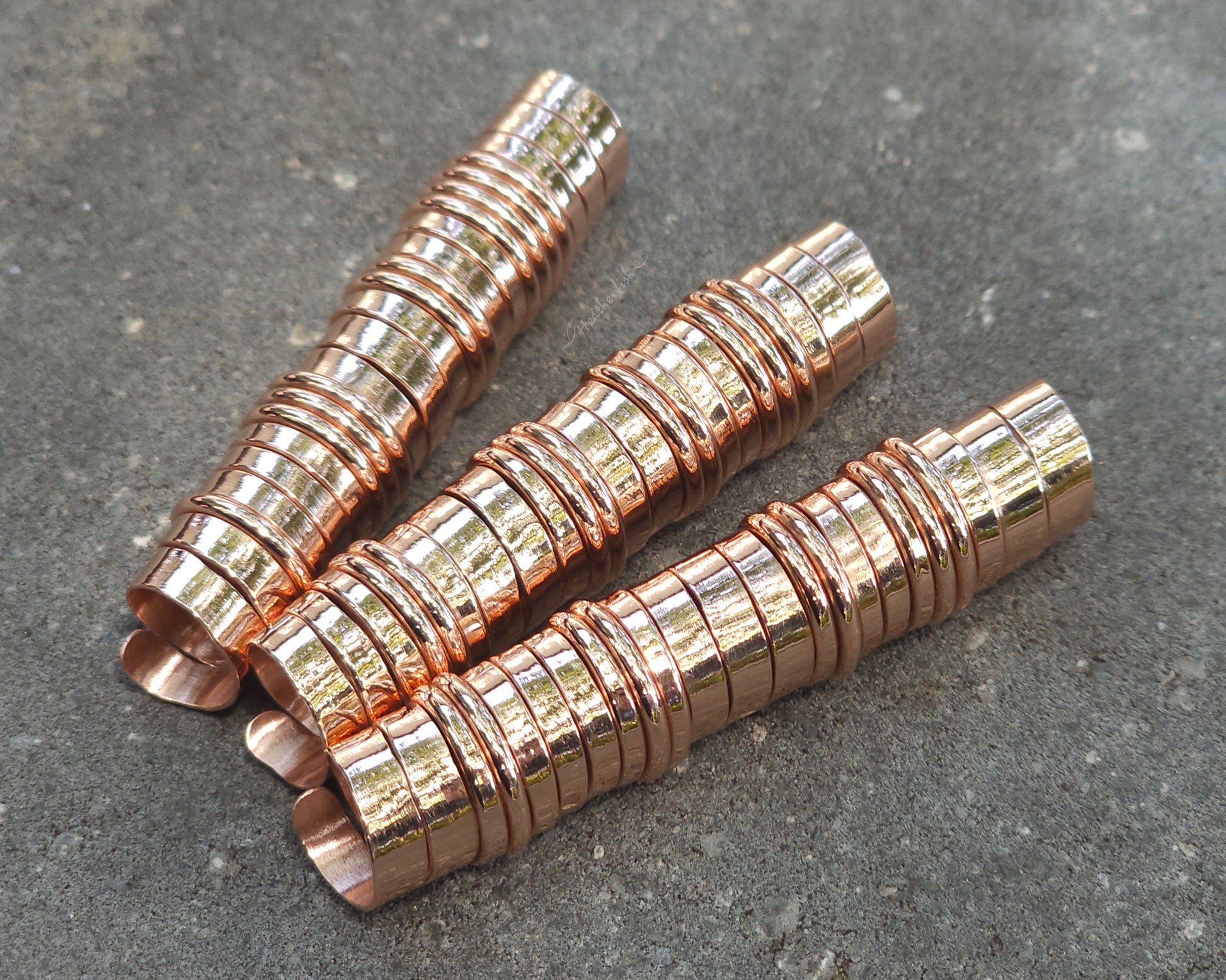 Three extra long copper hair coils on stone background.