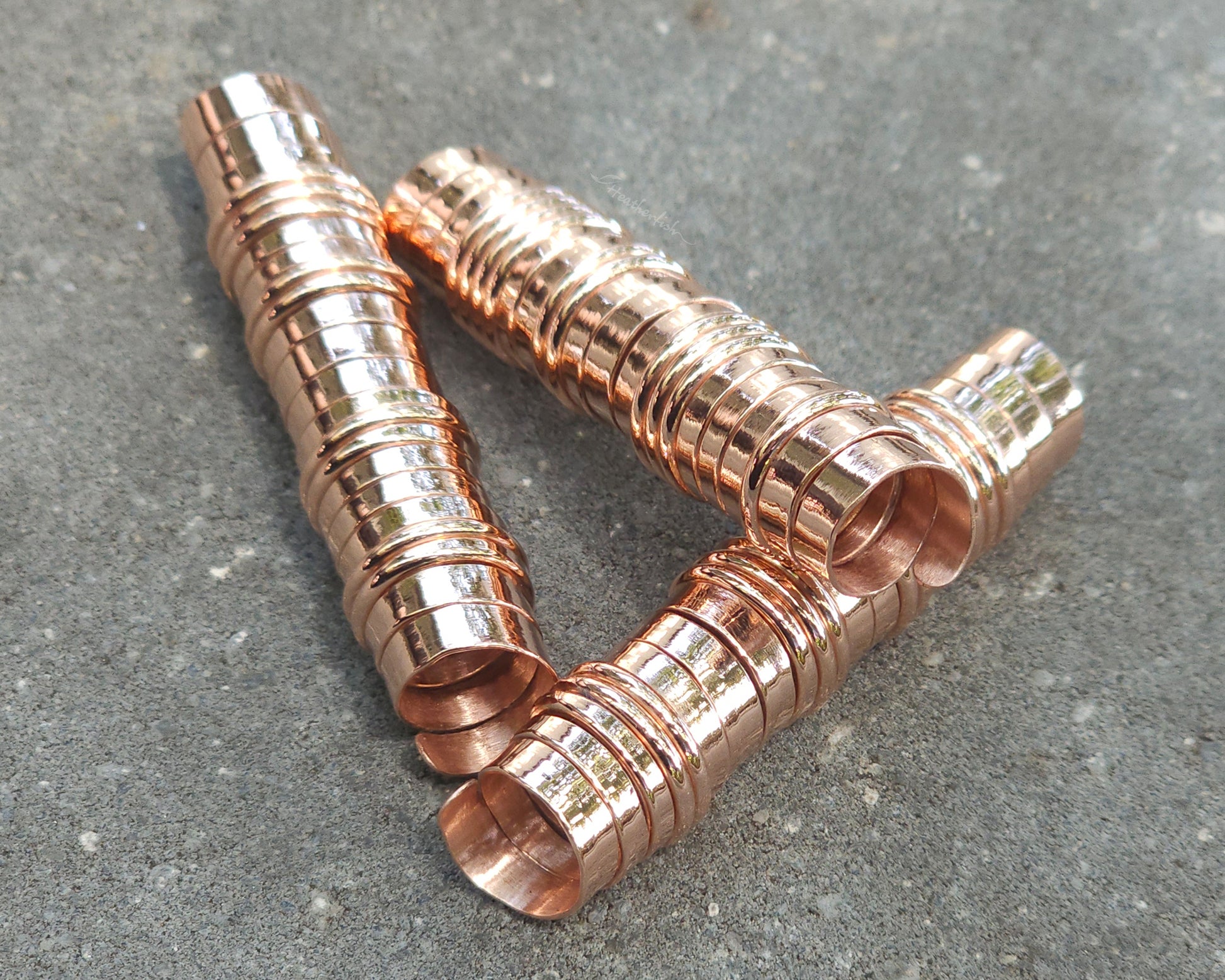 Three extra long copper hair coils on stone background.