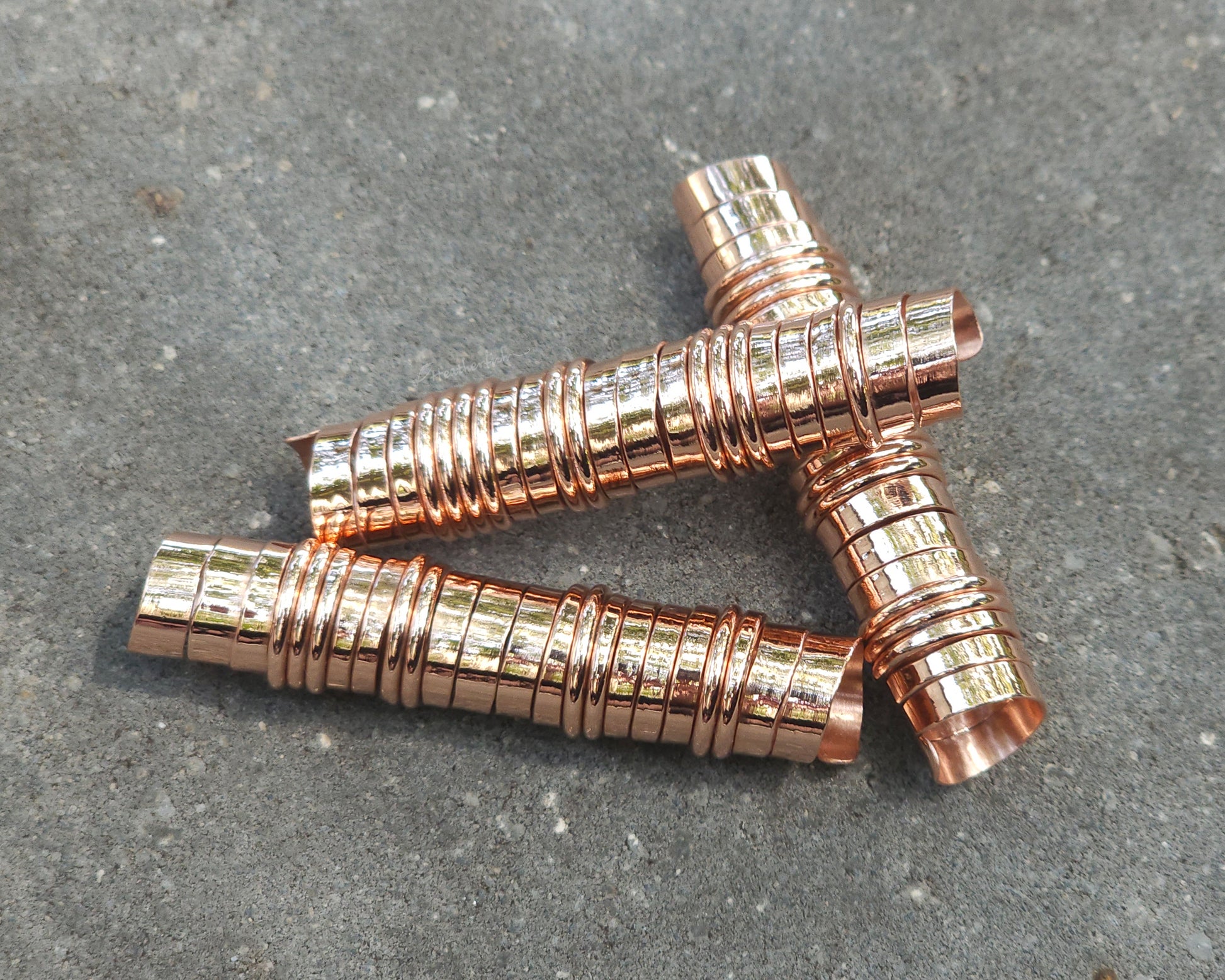 Three extra long copper hair coils on stone background.