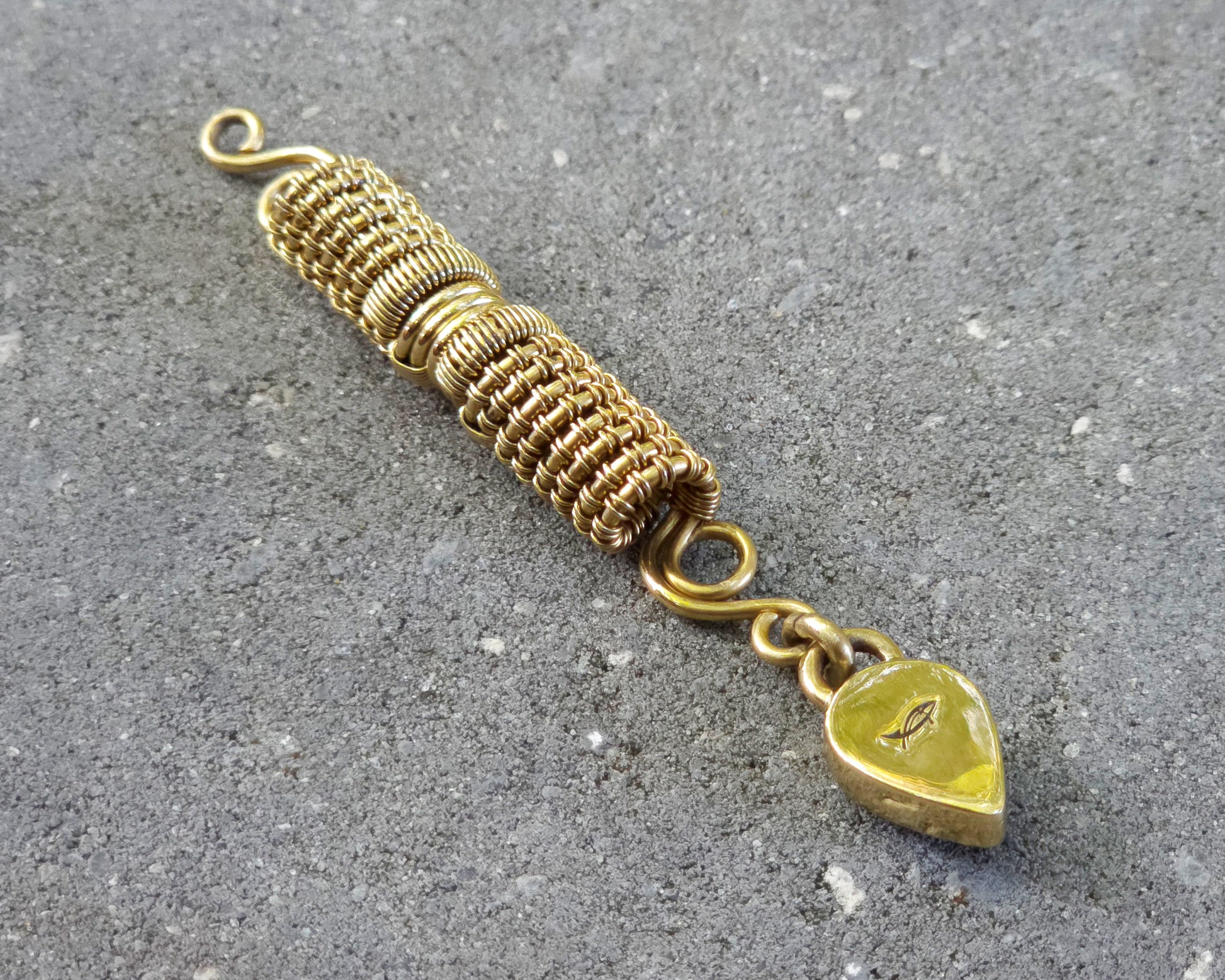 A handmade gold tone wire-wrapped hair bead with a teardrop-shaped blue lapis lazuli stone, displayed so the back of the pendant shows the heatherfish maker's mark on a textured gray concrete surface.