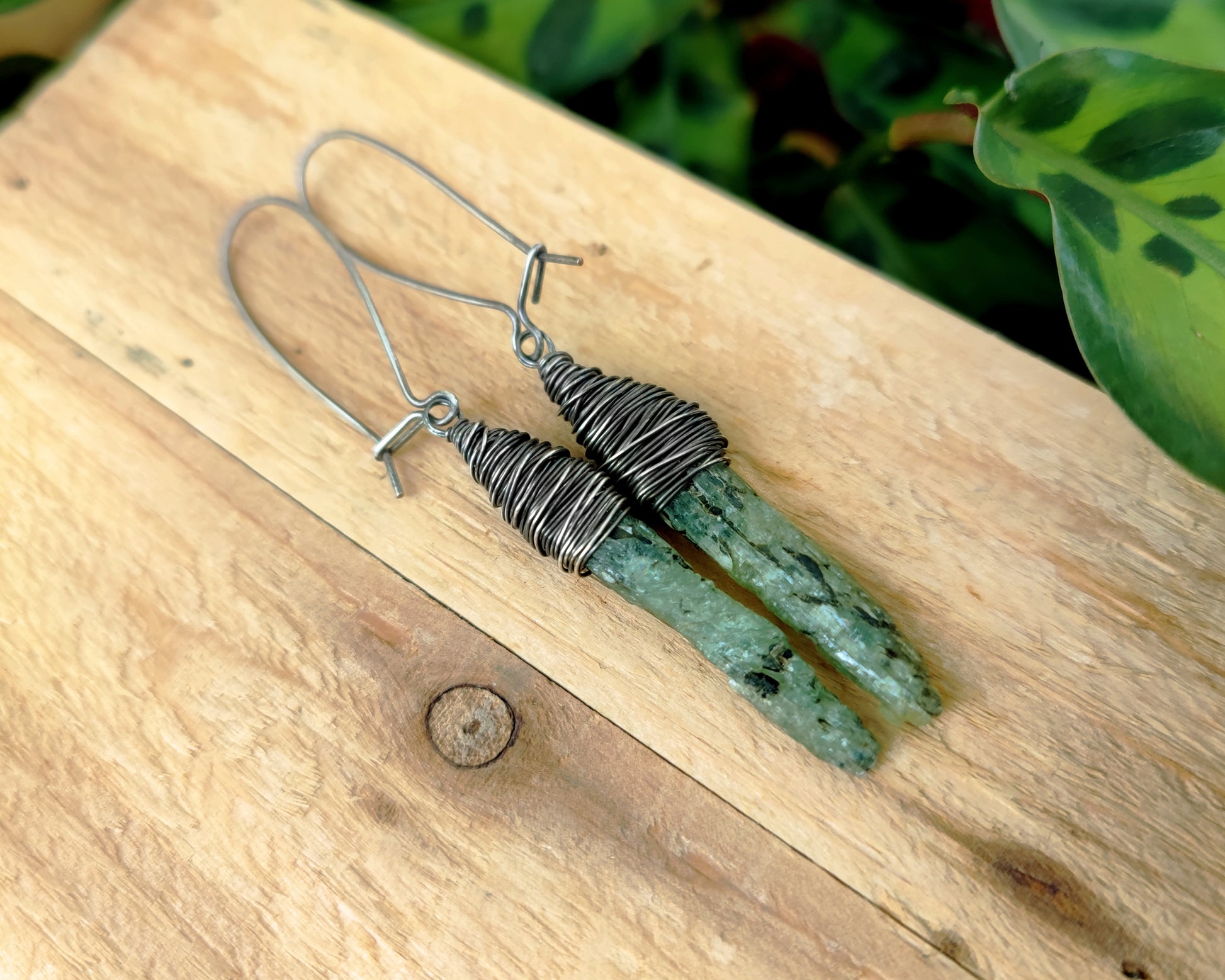 Silver green kyanite earrings on a wood background.