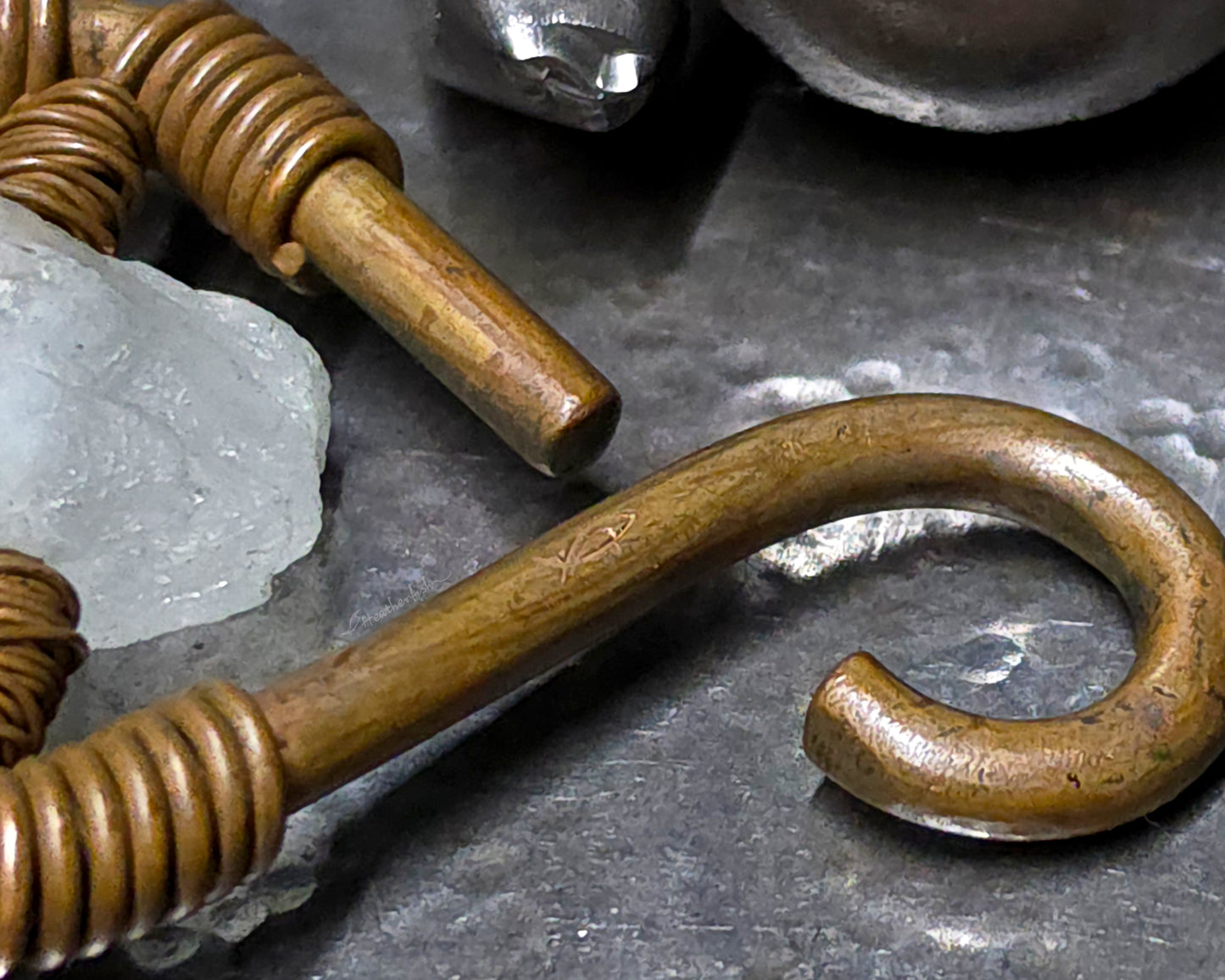 Close up of a heatherfish maker's mark on the copper curve of an ear weight on a wood background.