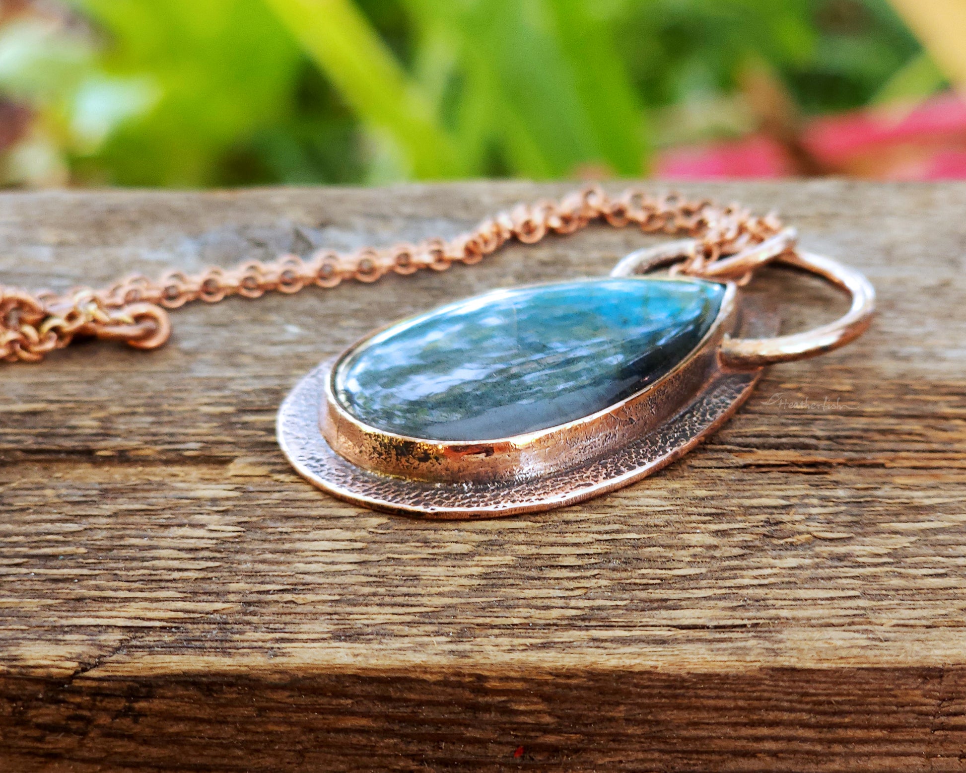 Necklace with a teardrop-shaped gemstone pendant on a wooden surface with a blurred natural background