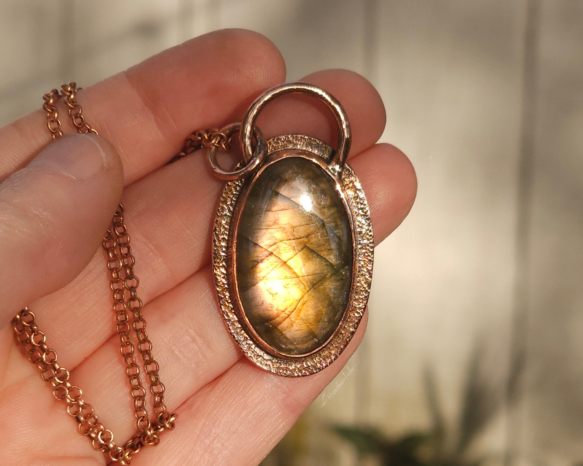 Copper and labradorite pendant held in a hand against a blurred background