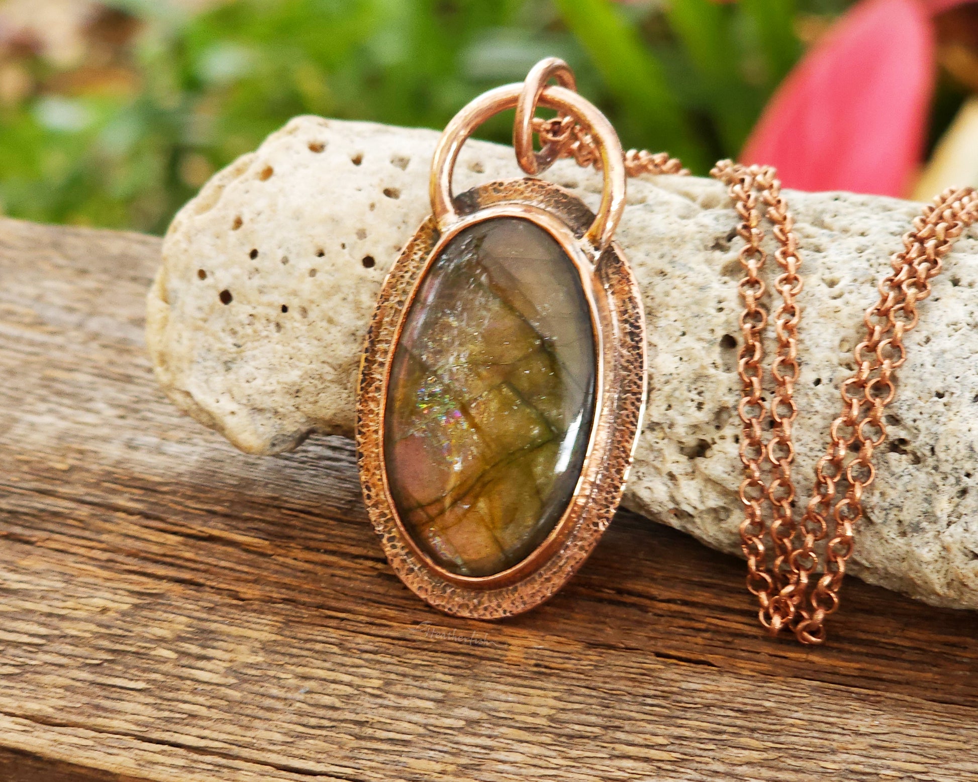 Copper pendant with embedded labradorite stone on a wooden surface