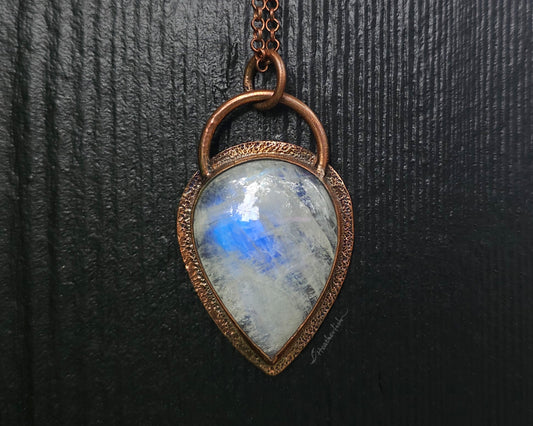 Necklace with a teardrop-shaped pendant featuring a blue moonstone on a dark textured background