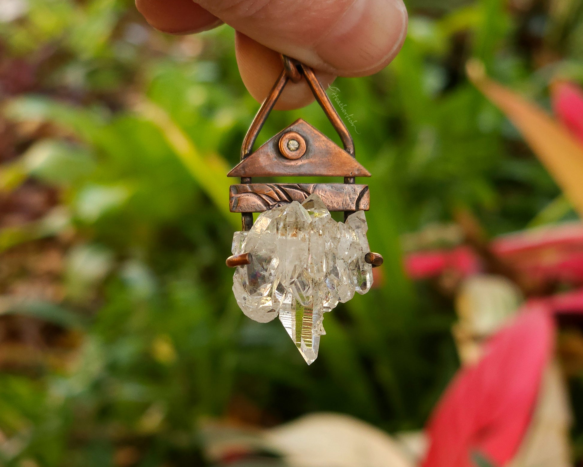 Crystal pendant with copper accents held against a natural background