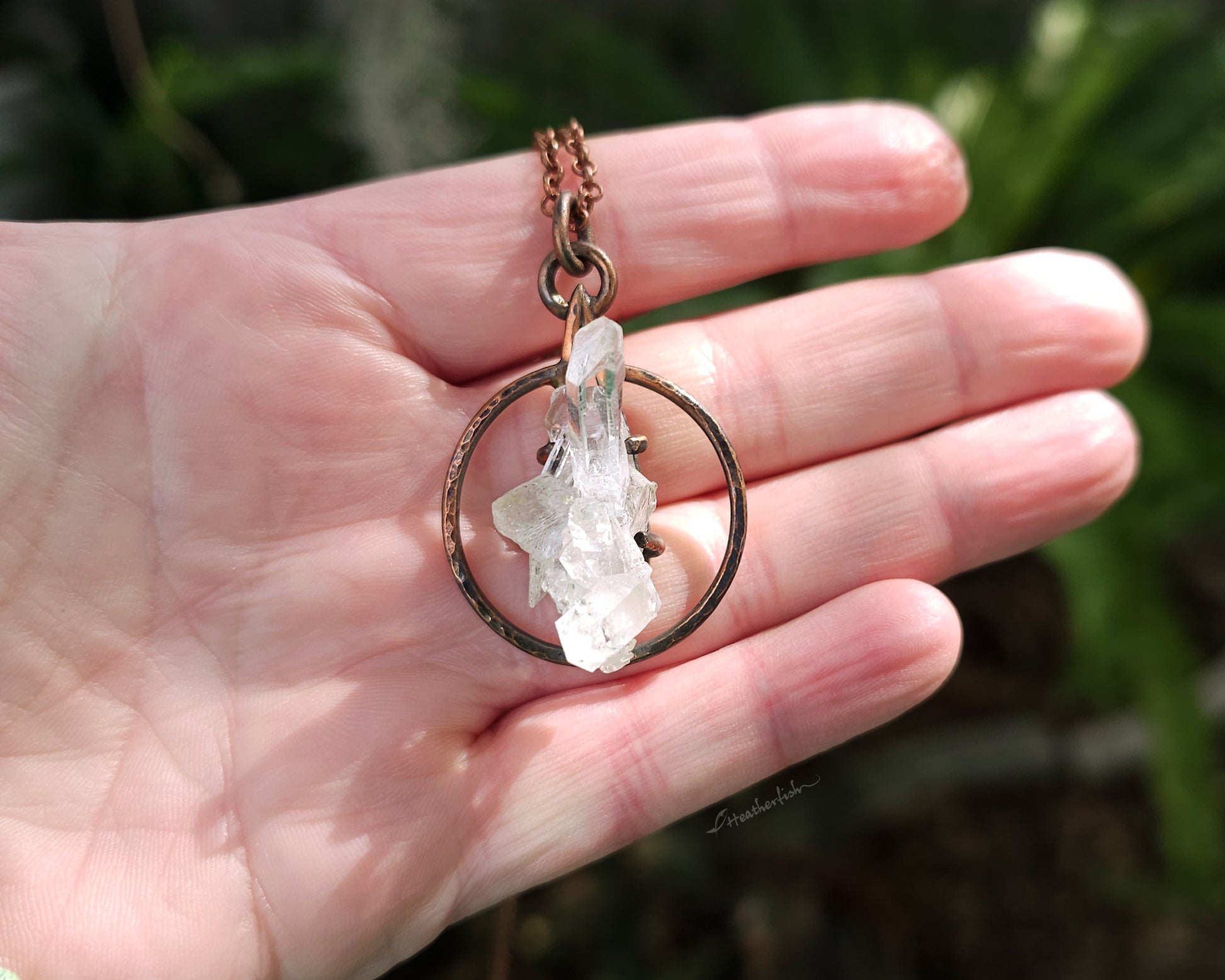 Necklace with a crystal pendant held in a hand against a natural background