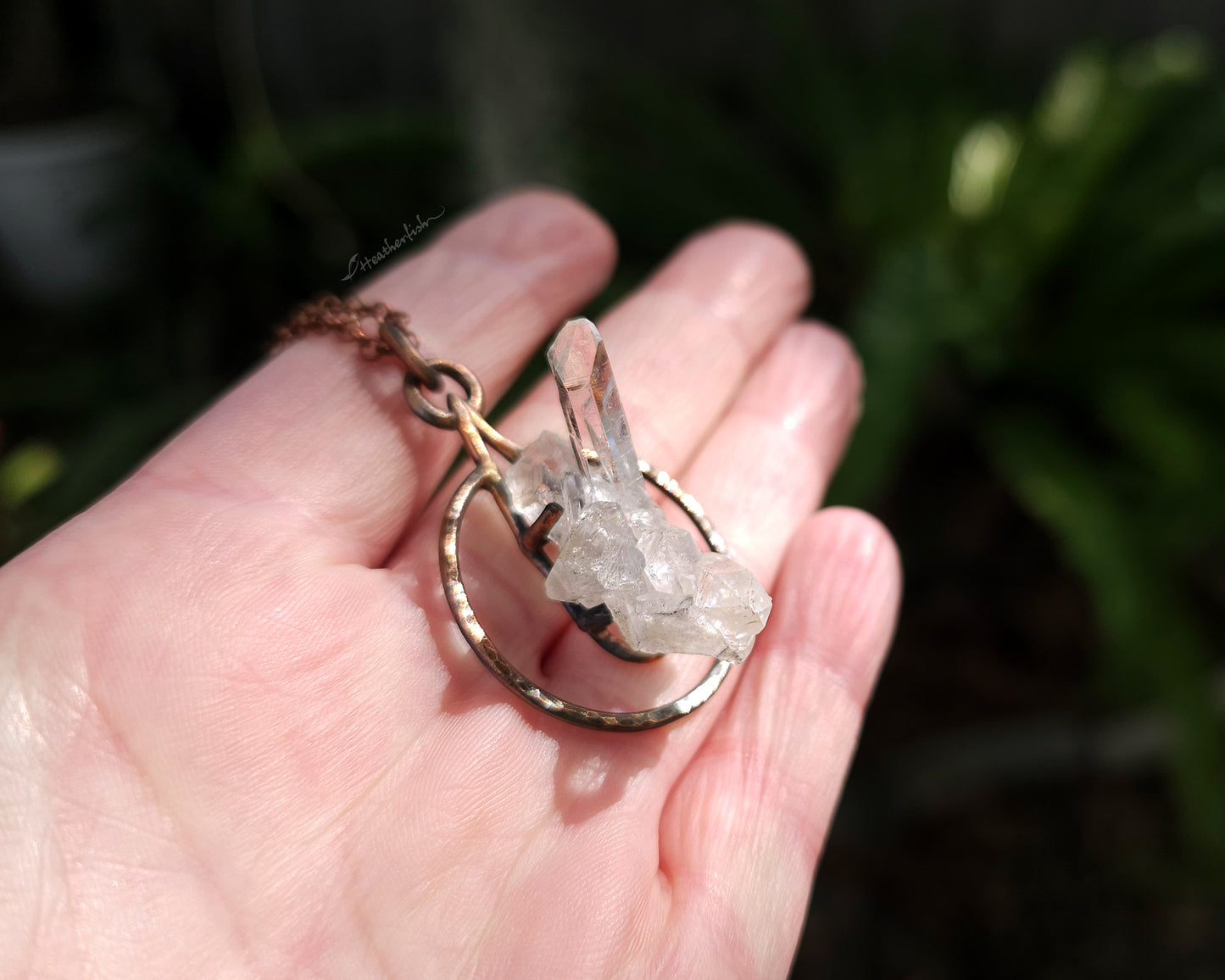 Hand holding a crystal pendant with a blurred natural background