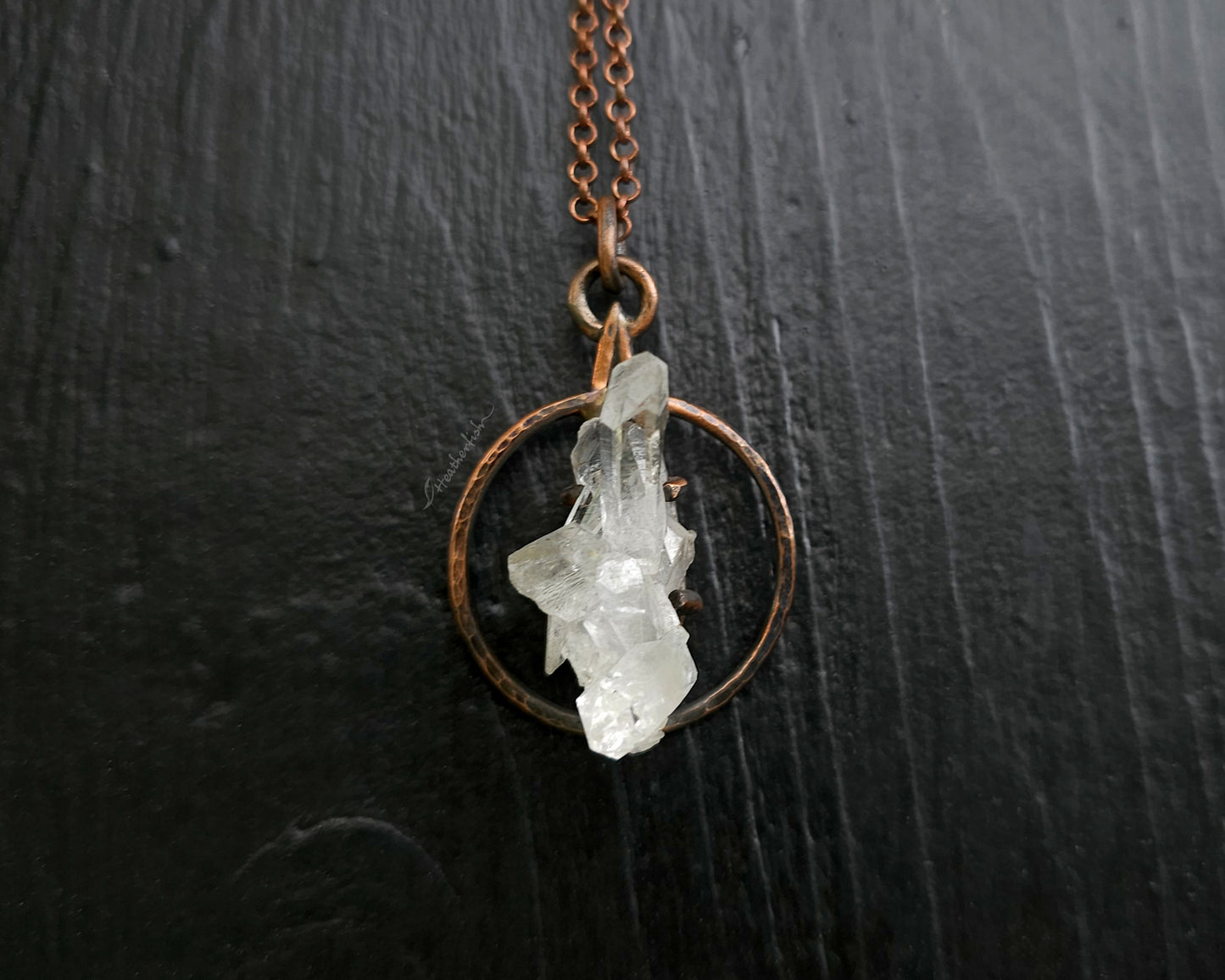 Necklace with a copper chain and crystal pendant on a dark surface