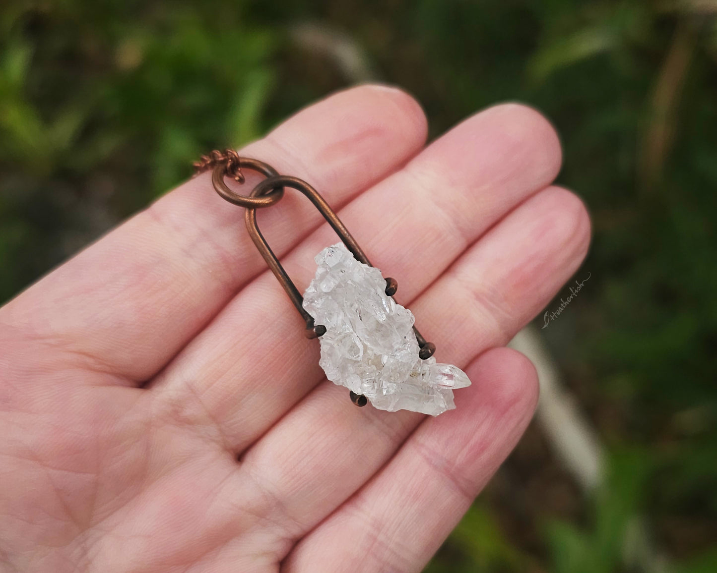 Quartz cluster necklace held in hand with blurred natural background.