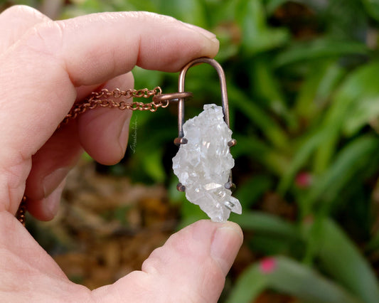 Quartz cluster necklace held in hand with blurred natural background.