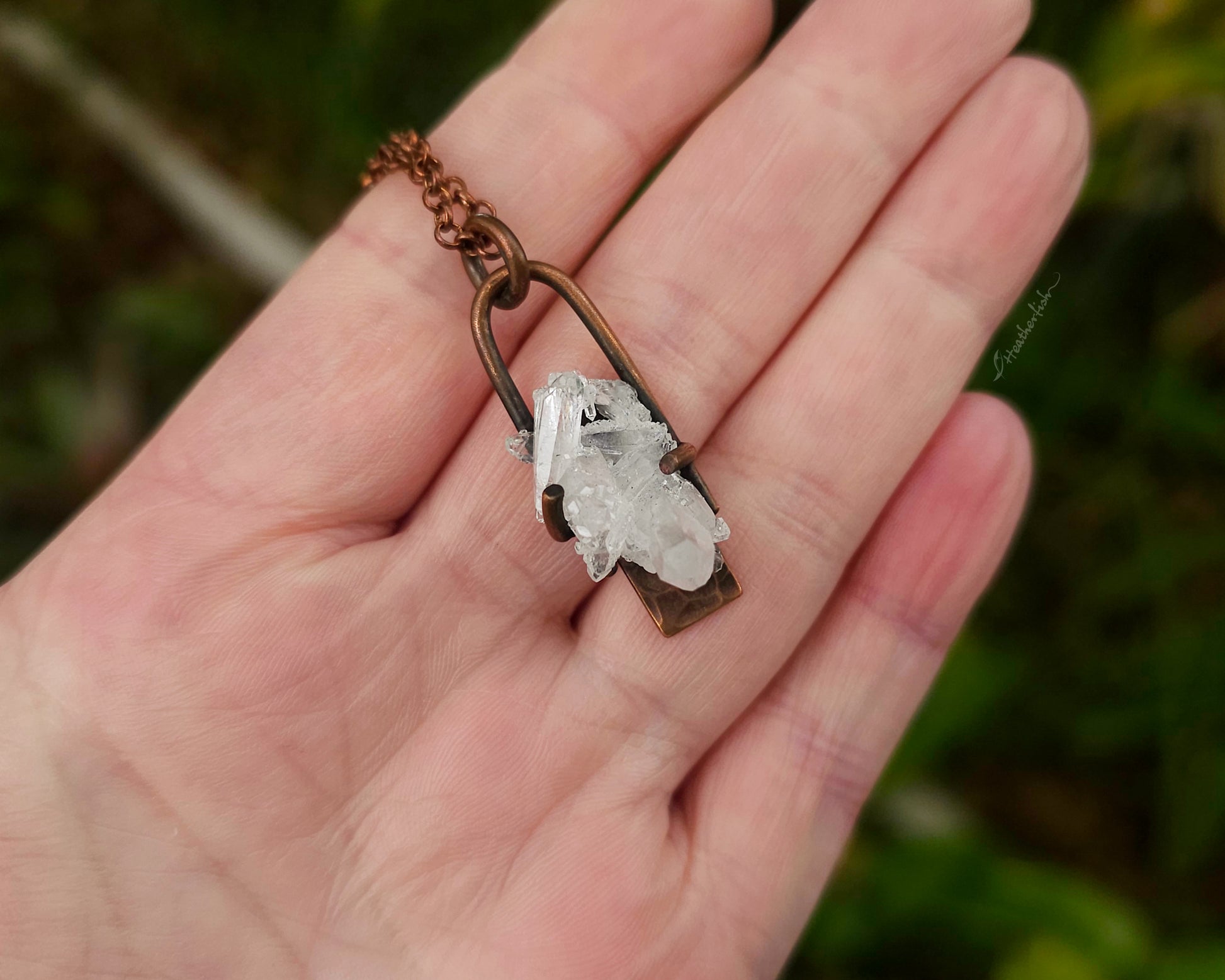 Crystal pendant on a chain held in a hand with a wooden background
