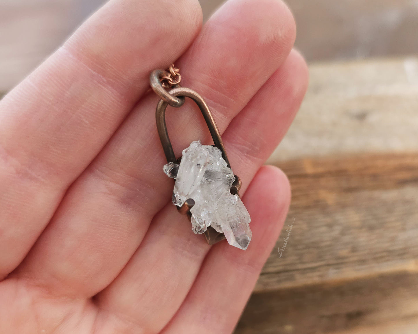 Crystal pendant on a chain held in a hand with a wooden background