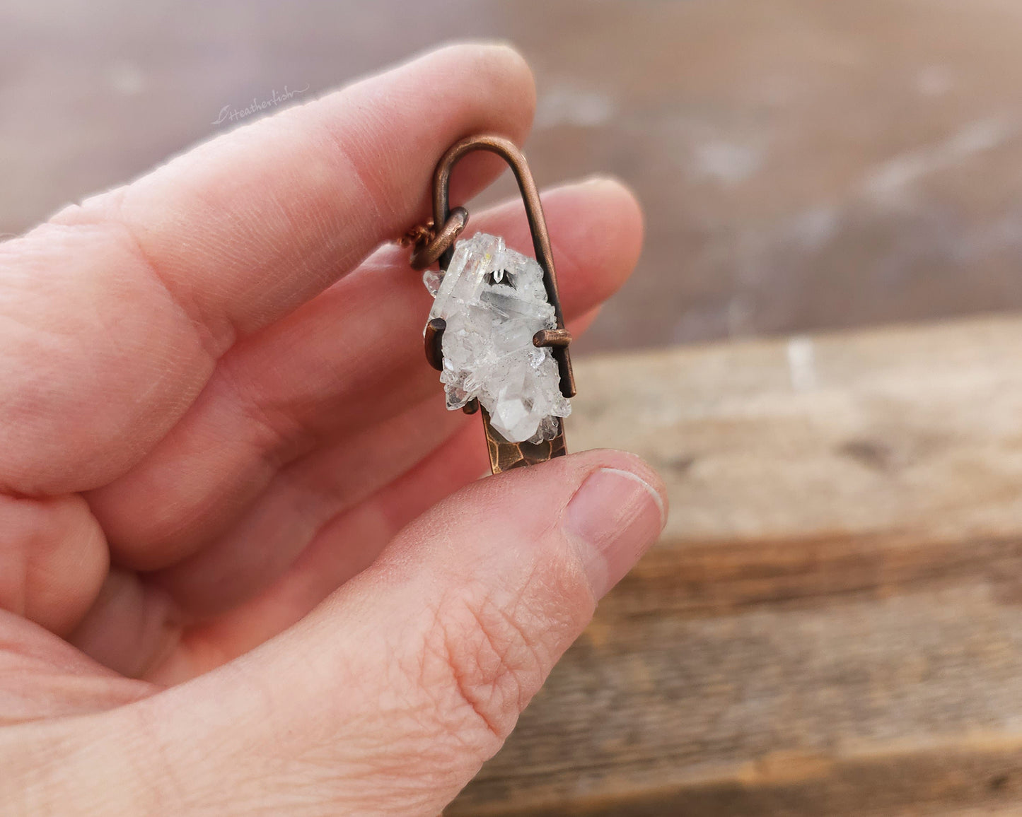 Crystal pendant on a chain held in a hand with a wooden background