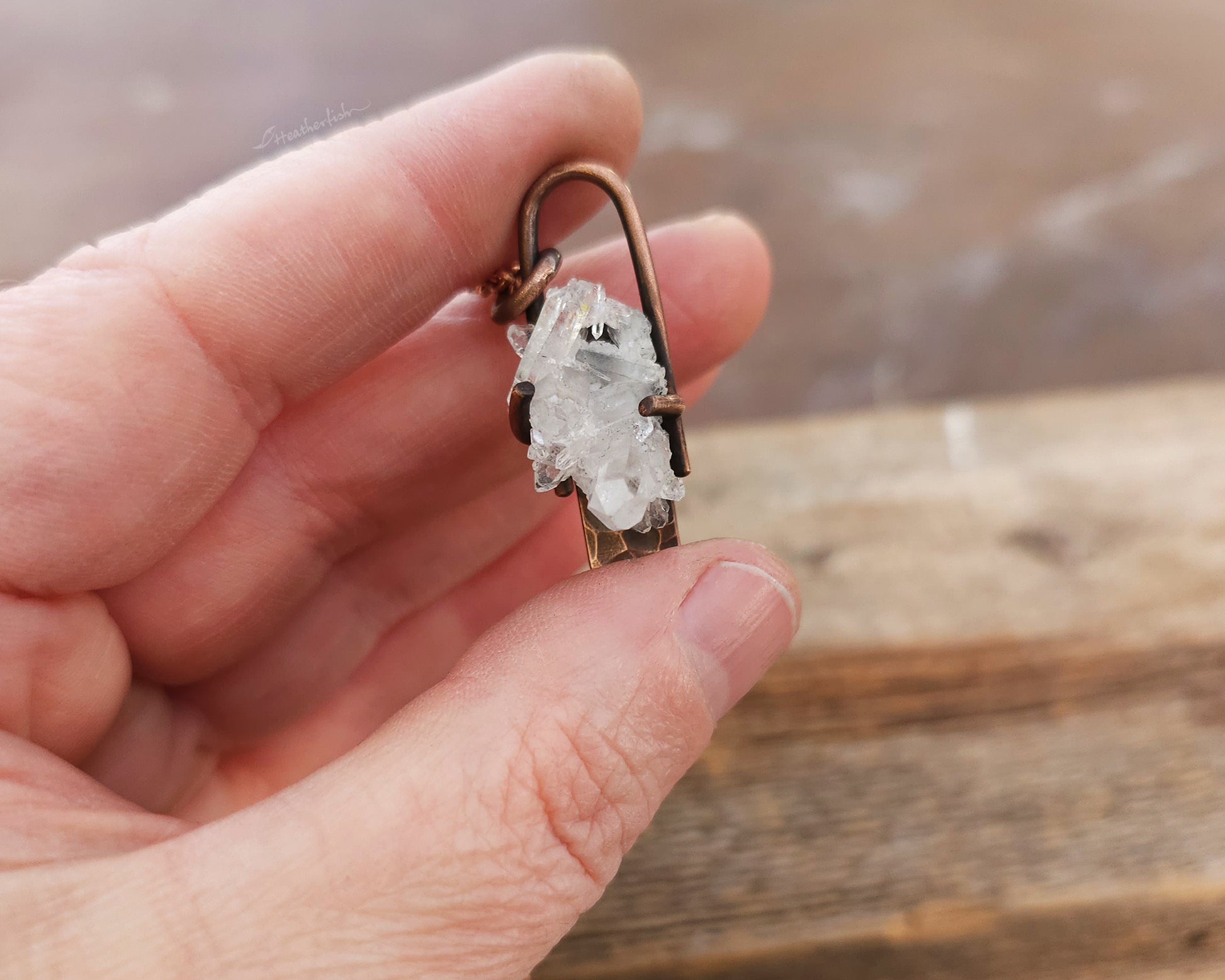 Crystal pendant on a chain held in a hand with a wooden background