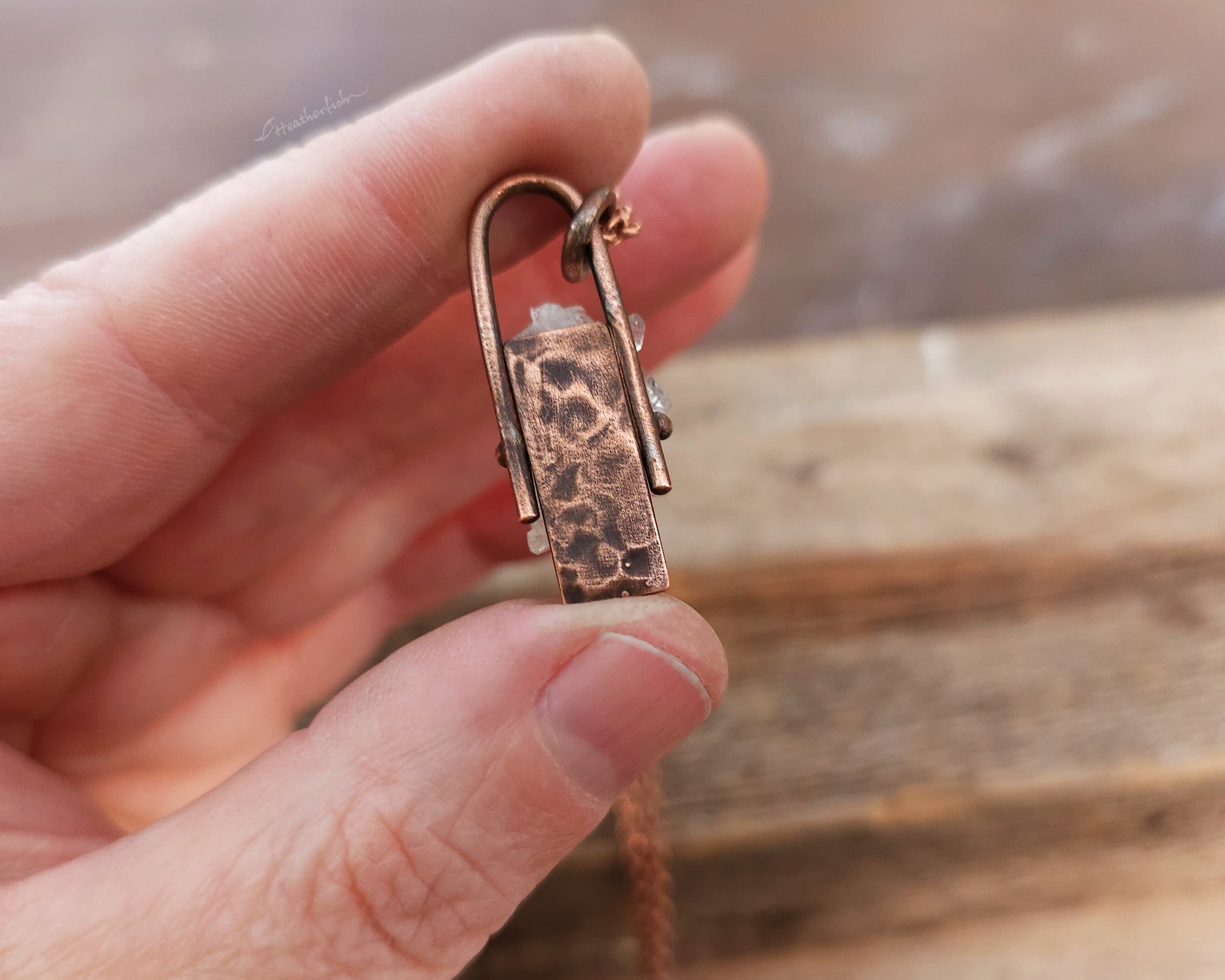 Crystal pendant on a chain held in a hand with a wooden background