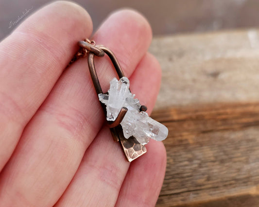 Crystal pendant on a chain held in a hand with a wooden background
