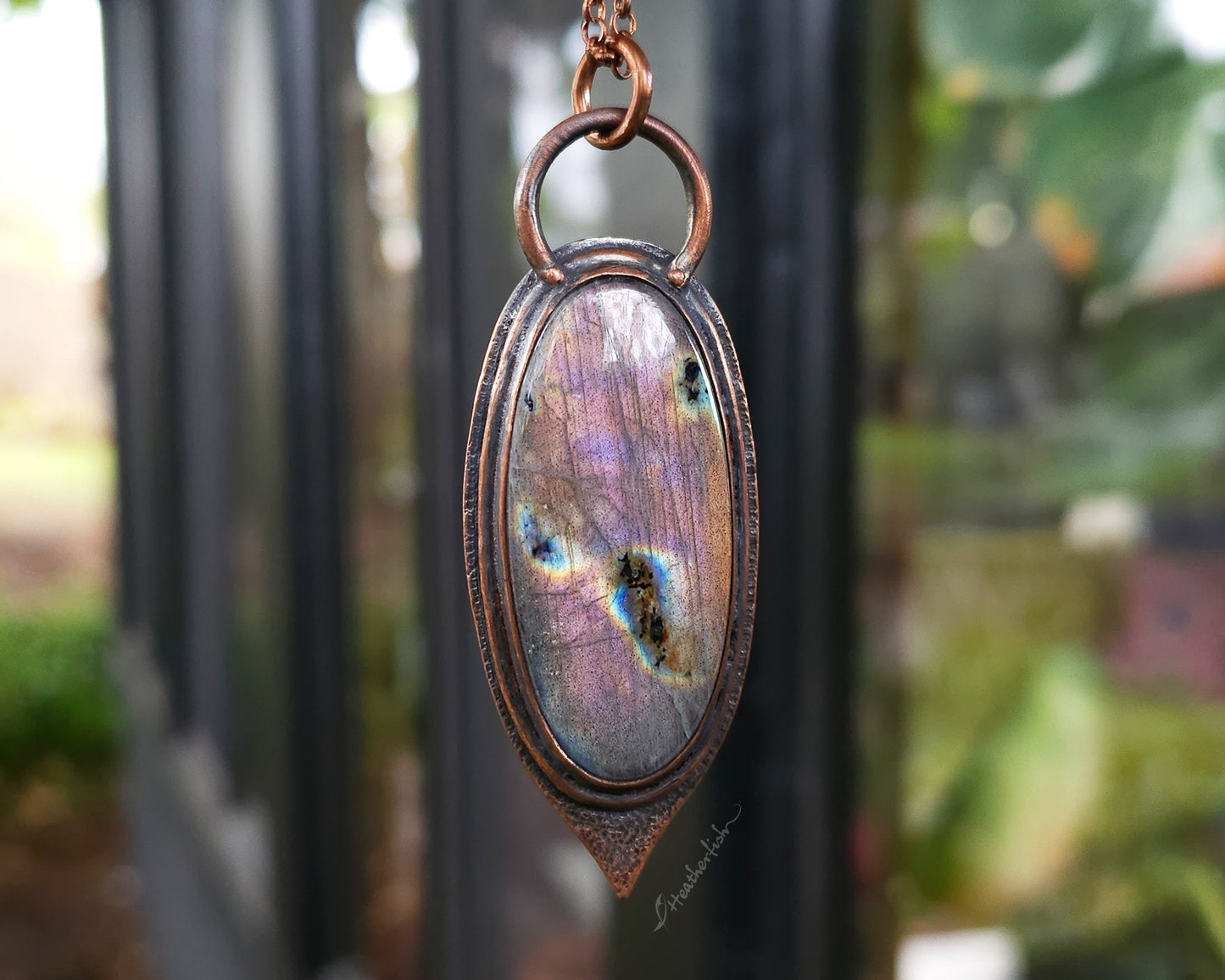 Necklace with a pendant featuring a colorful stone against a blurred outdoor background