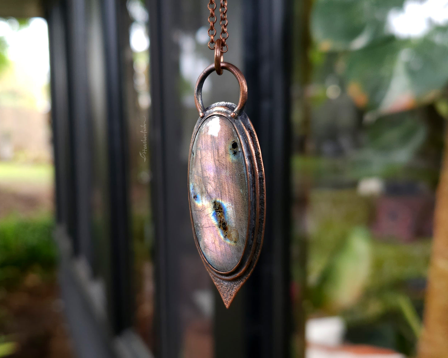 Copper pendant with a colorful stone on a blurred outdoor background