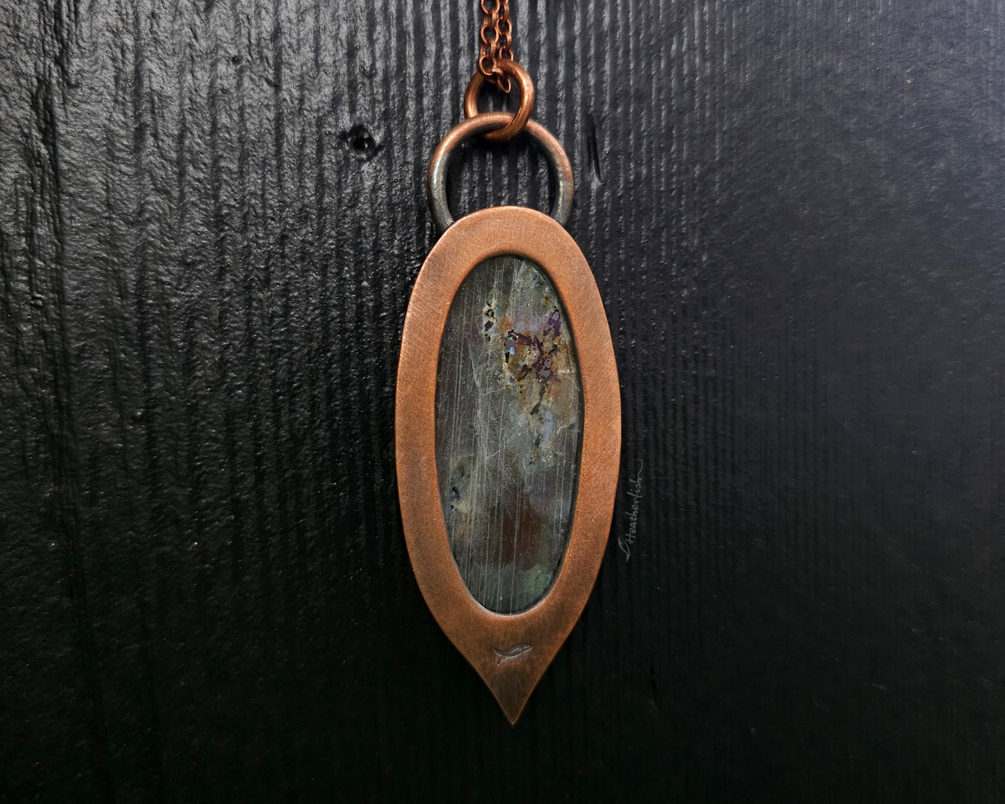 Copper pendant with a natural stone inset on a dark textured background