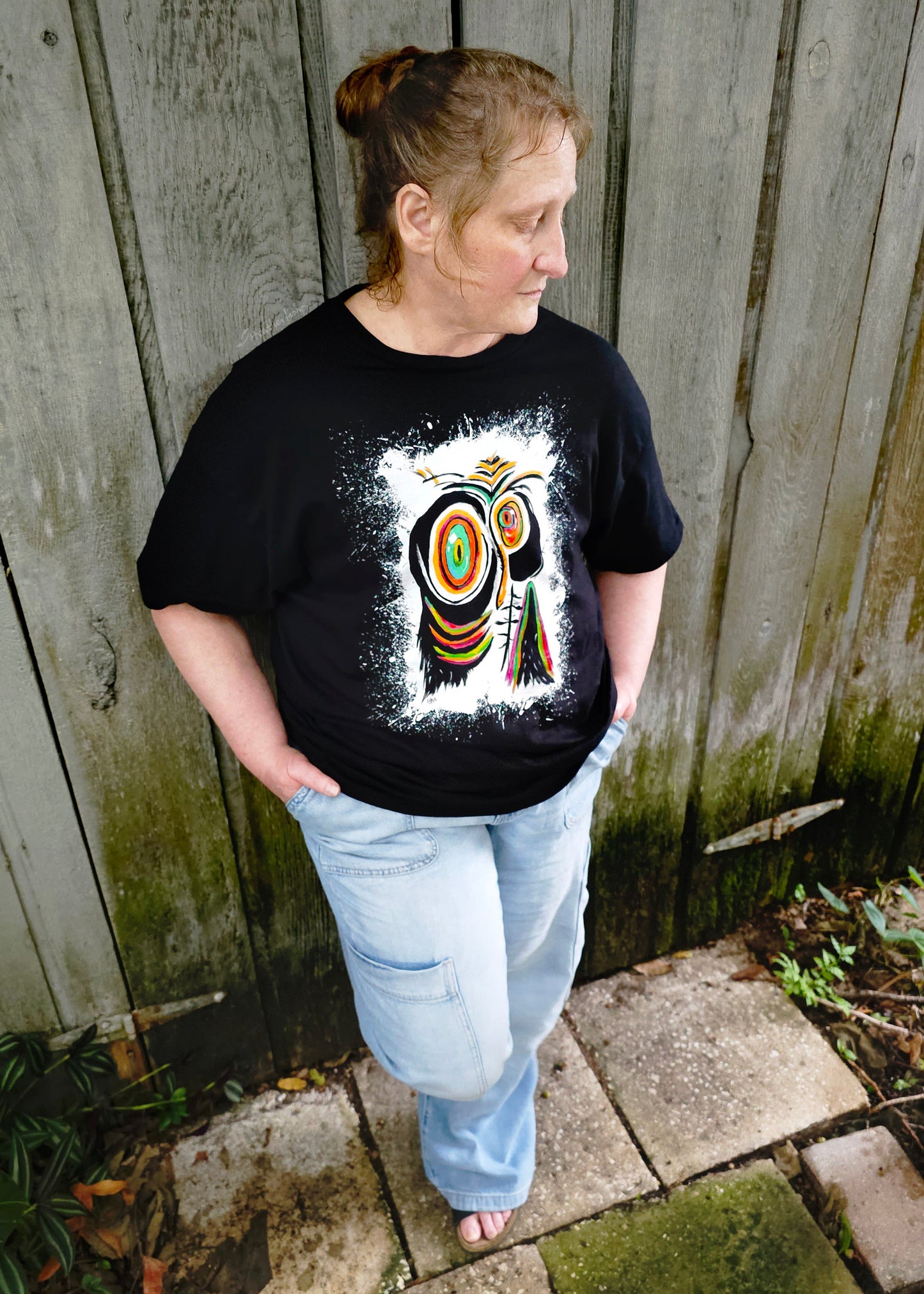 A woman wearing a pair of jeans and the sad penguin artisan t-shirt standing next to a rustic shiplap wall.