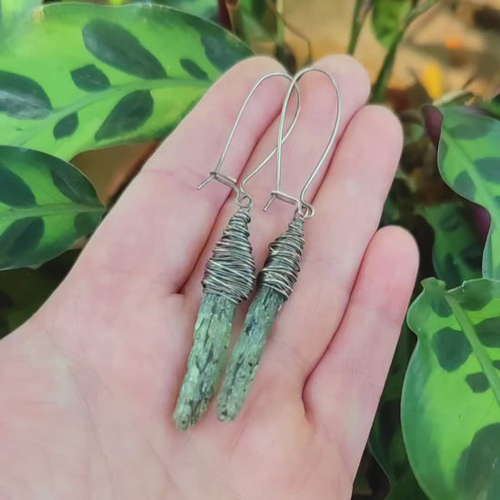 Pair of green kyanite earrings held in hand.