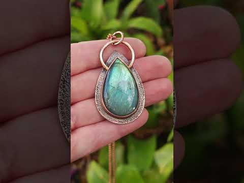A pear-shaped aqua green labradorite pendant set in copper bezel. Held in hand to show labradorescence. 